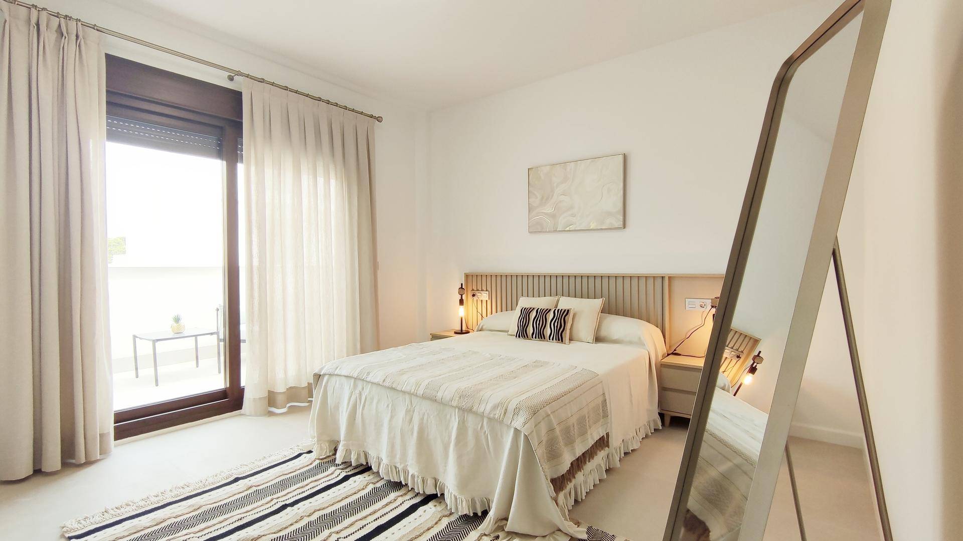 Helles Schlafzimmer mit Doppelbett, großem Spiegel und Zugang zu einem Balkon.