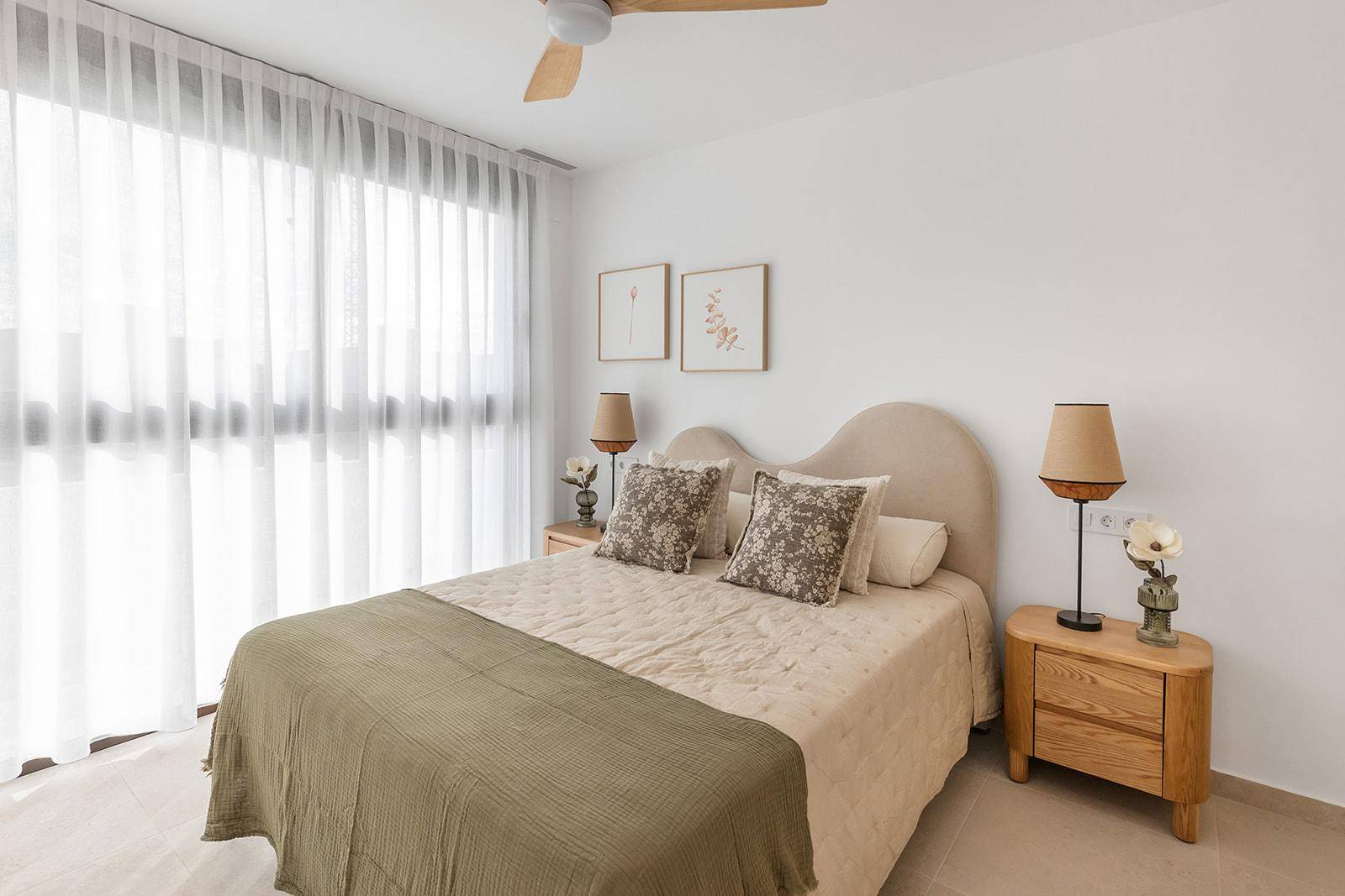 Helles Schlafzimmer mit großem Fenster, Deckenventilator und beigem Doppelbett.
