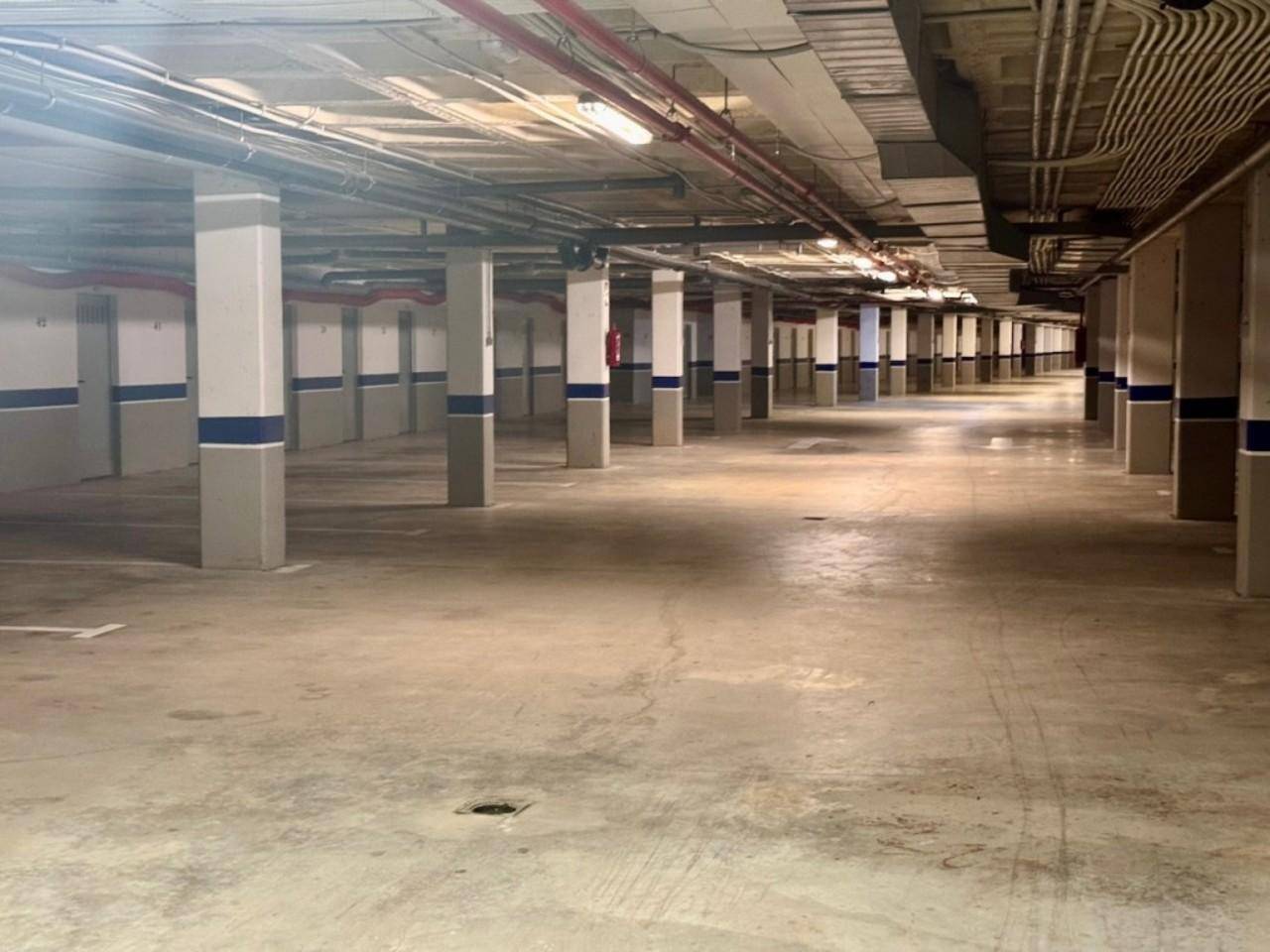 Geräumige Tiefgarage mit vielen Stellplätzen und sichtbaren Versorgungsleitungen an der Decke.