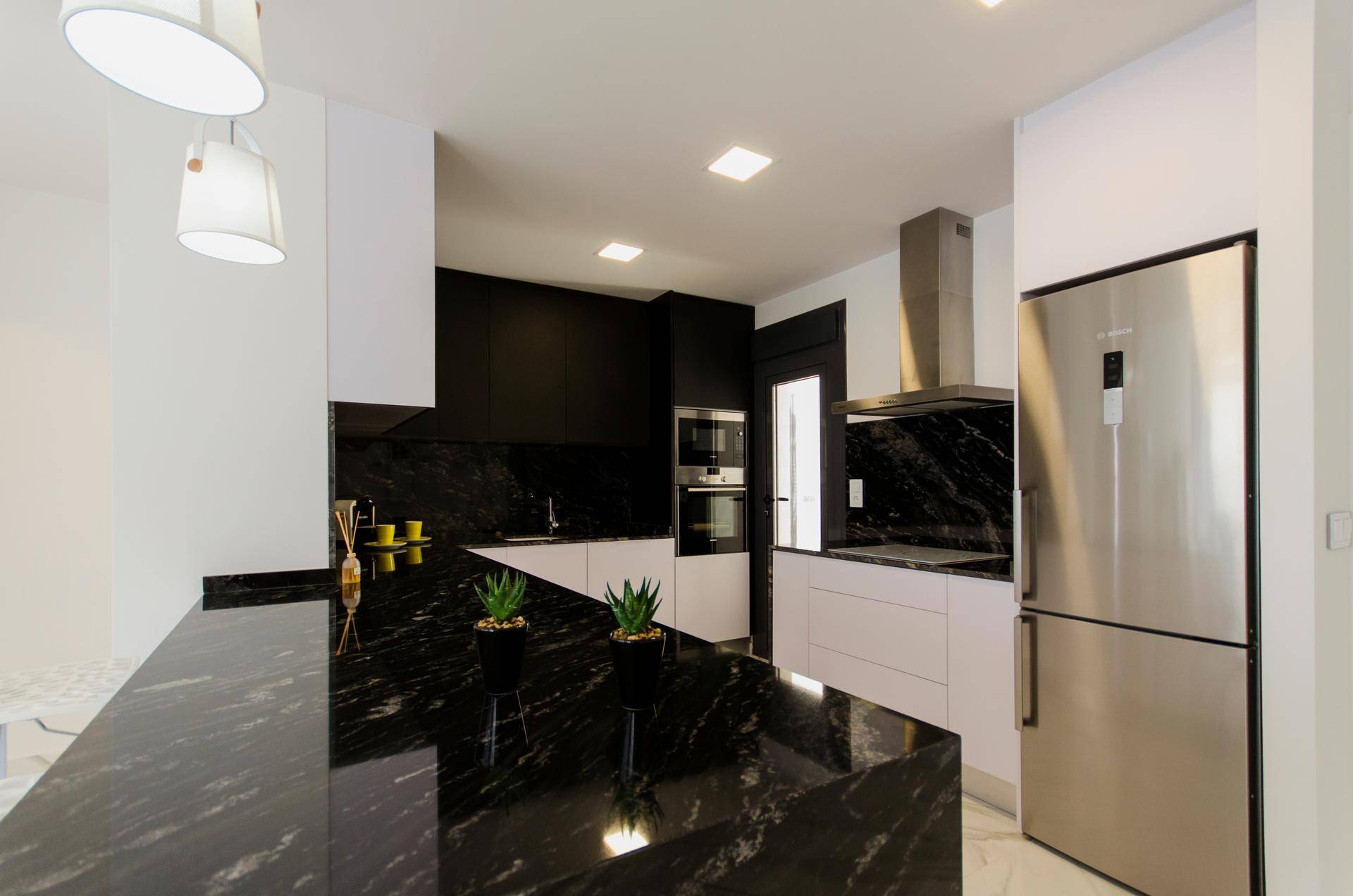 Moderne Küche mit schwarzer Granit-Arbeitsplatte, weißen Unterschränken und integrierten Geräten.