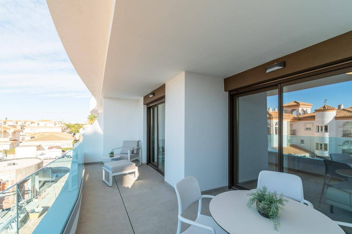 Großer Balkon mit Ess- und Lounge-Möbeln, Glasgeländer und Zugang zu zwei Innenräumen.