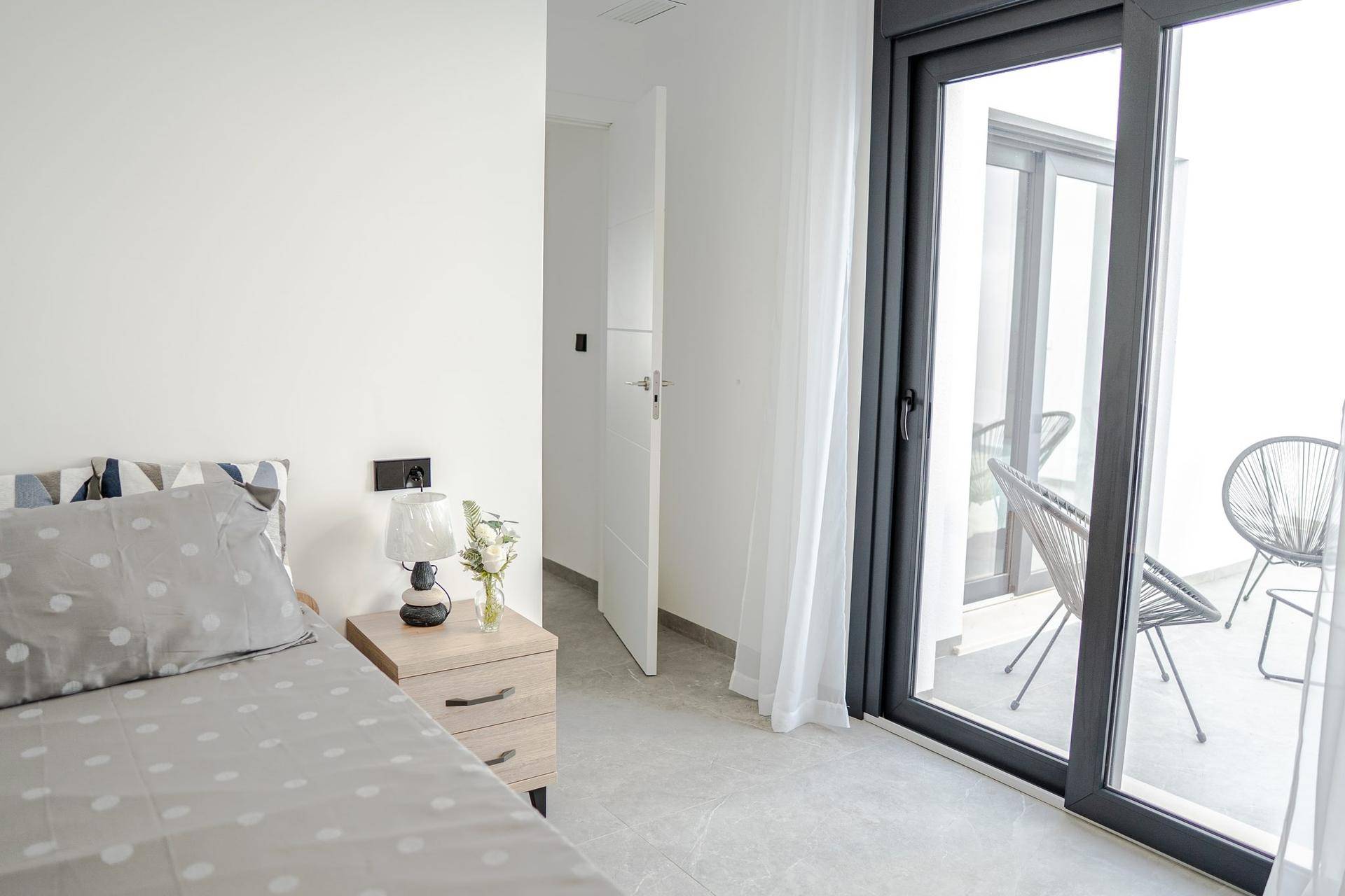 Schlafzimmer mit Nachttisch, Lampe und Schiebetür, die zu einem Balkon oder einer Terrasse führt.
