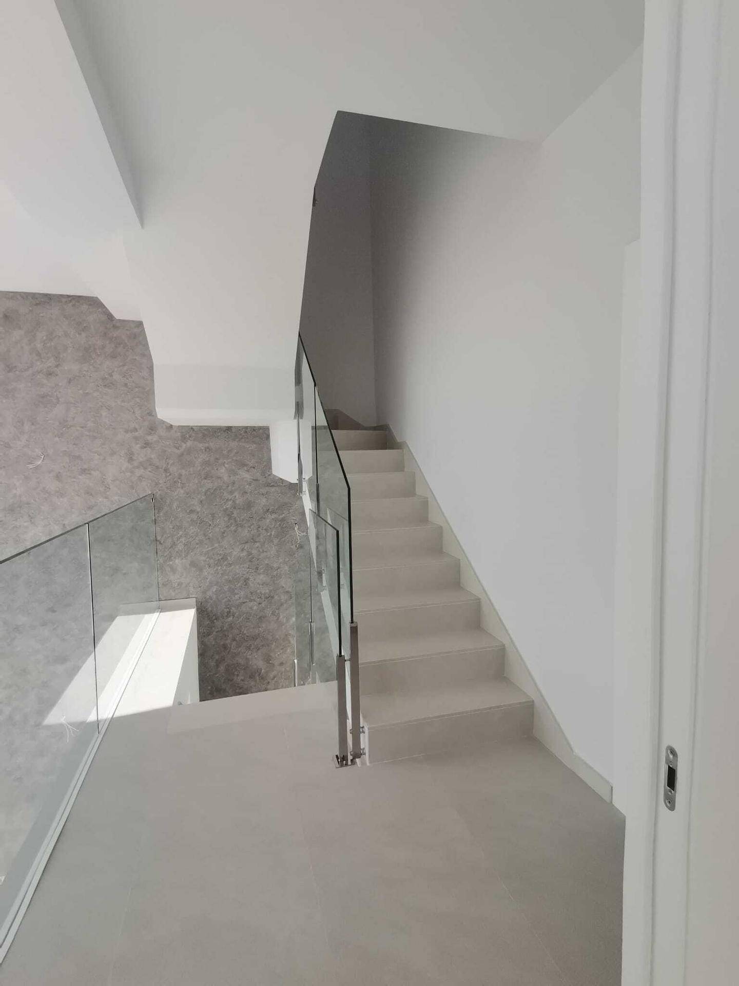 Moderne Treppe mit Glasgeländer und hellem Fliesenboden, die die Etagen elegant verbindet.