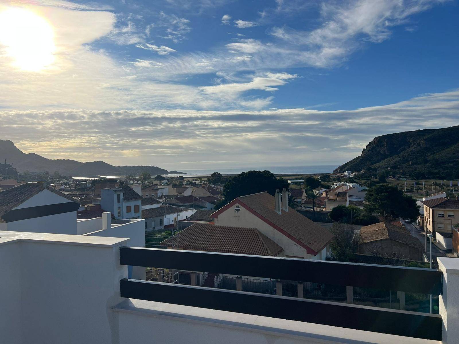 Weitläufiger Blick über eine Küstenstadt mit Meer und Bergen im Hintergrund bei Sonnenuntergang.