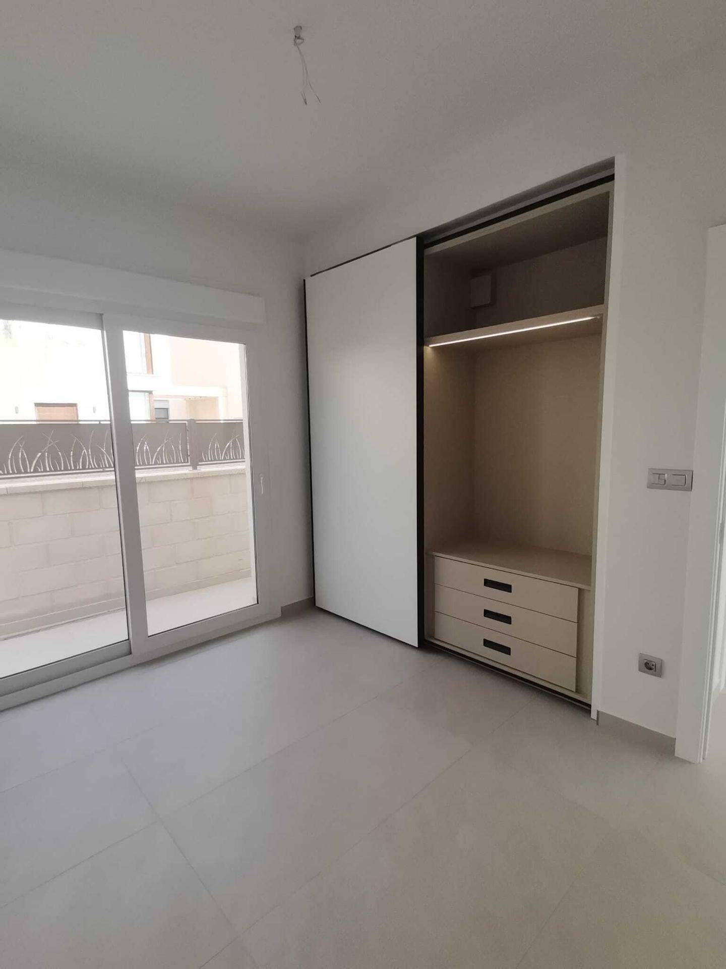 Helles Schlafzimmer mit offenem Einbauschrank und Zugang zum Balkon, ideal für Stauraum.