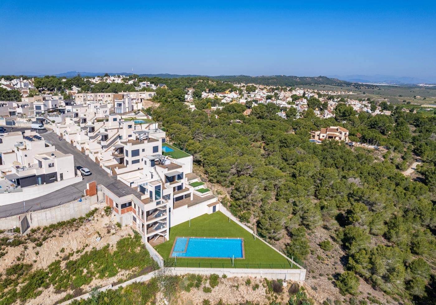 Luftaufnahme einer modernen Wohnanlage mit Pool und viel Grün in hügeliger Landschaft.