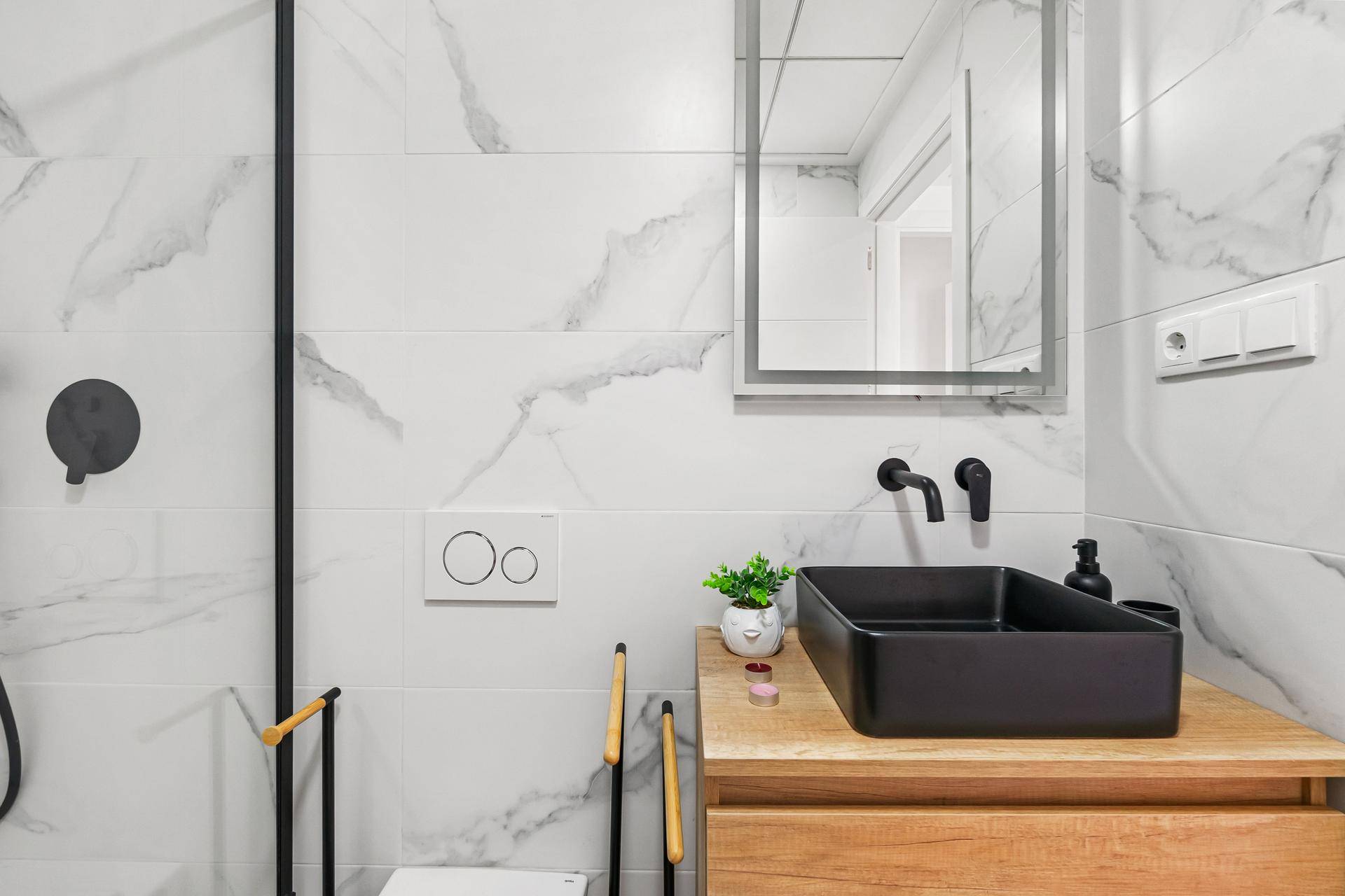 Modernes Badezimmer mit schwarzen Armaturen, schwarzem Waschbecken und weißen Marmorfliesen.