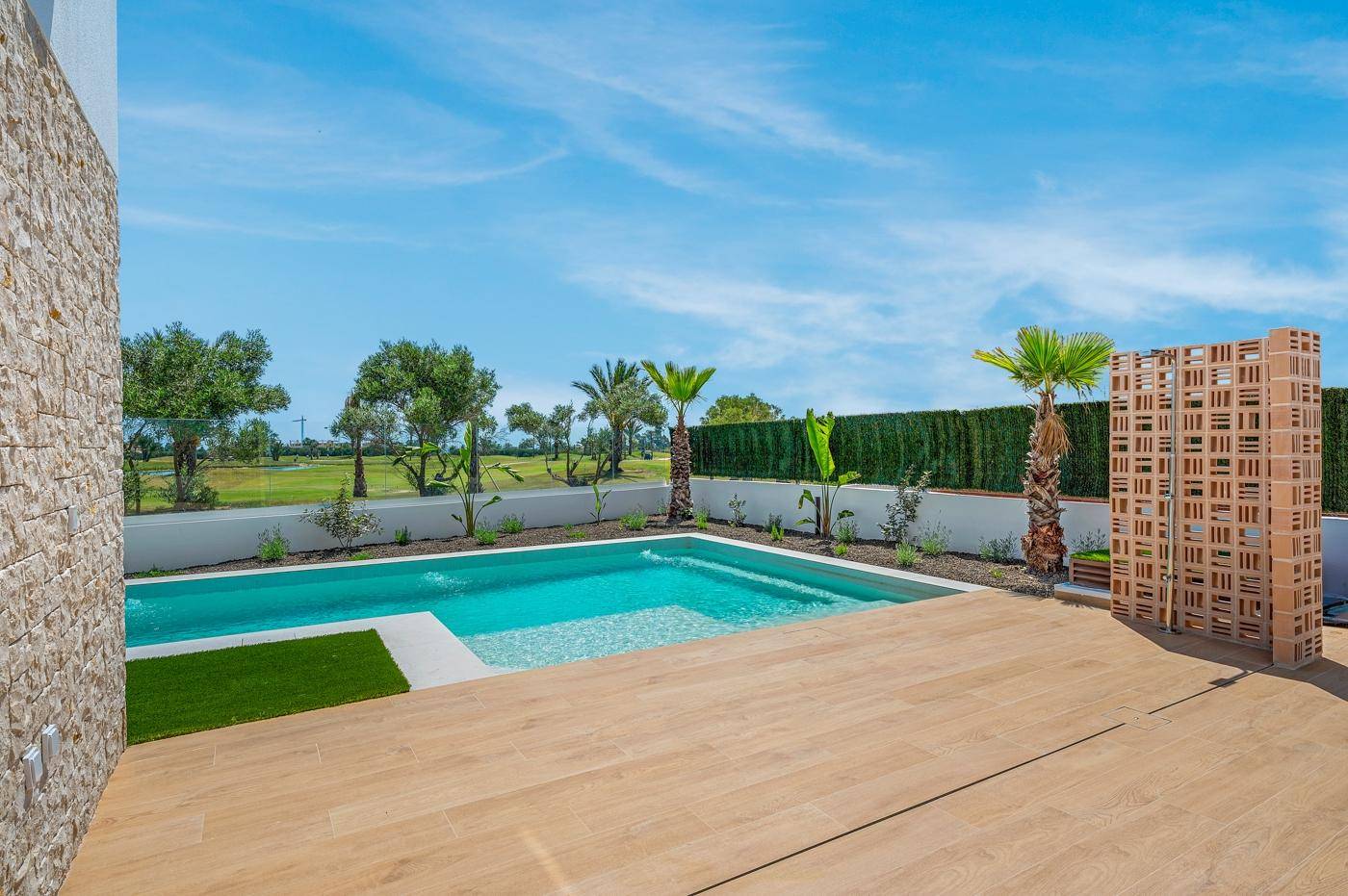 Entspannender Poolbereich mit Holzterrasse und Blick auf die grüne Landschaft an einem sonnigen Tag.