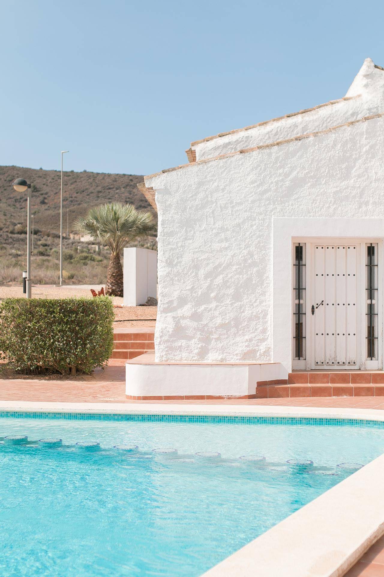 Weiß getünchtes Haus mit traditioneller Tür neben dem Gemeinschaftspool und mediterraner Bepflanzung.