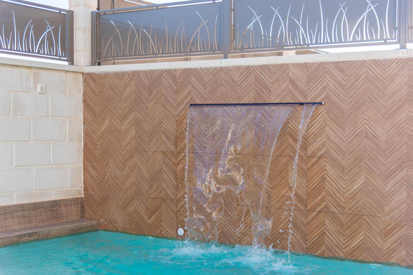 Detailansicht des Wasserfalls im Poolbereich mit dekorativer Wandverkleidung und klarem Wasser.