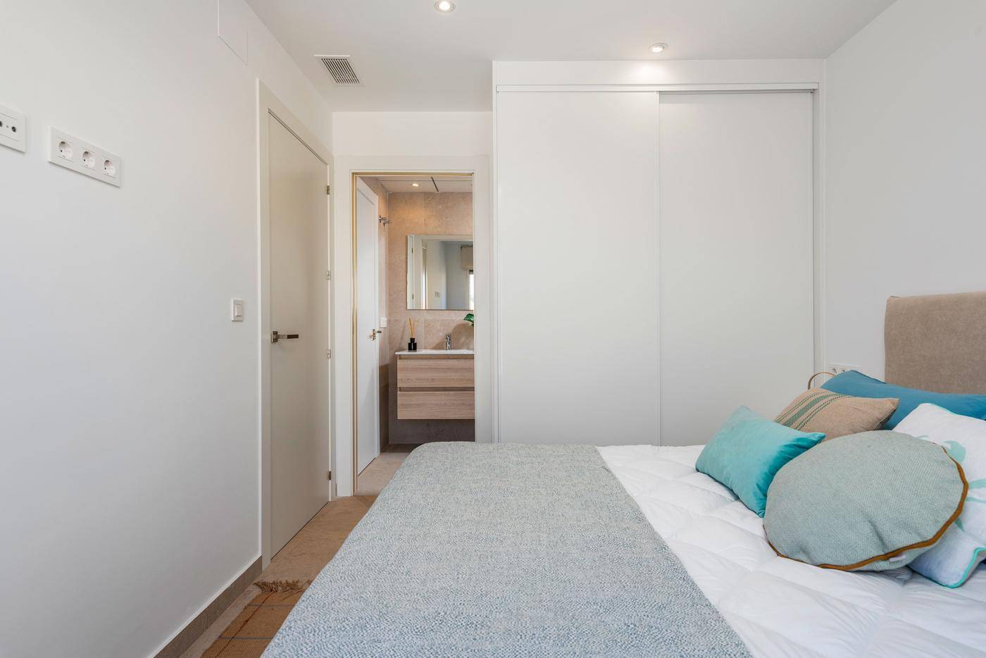 Schlafzimmer mit Einbauschrank und Zugang zu einem modernen Badezimmer.