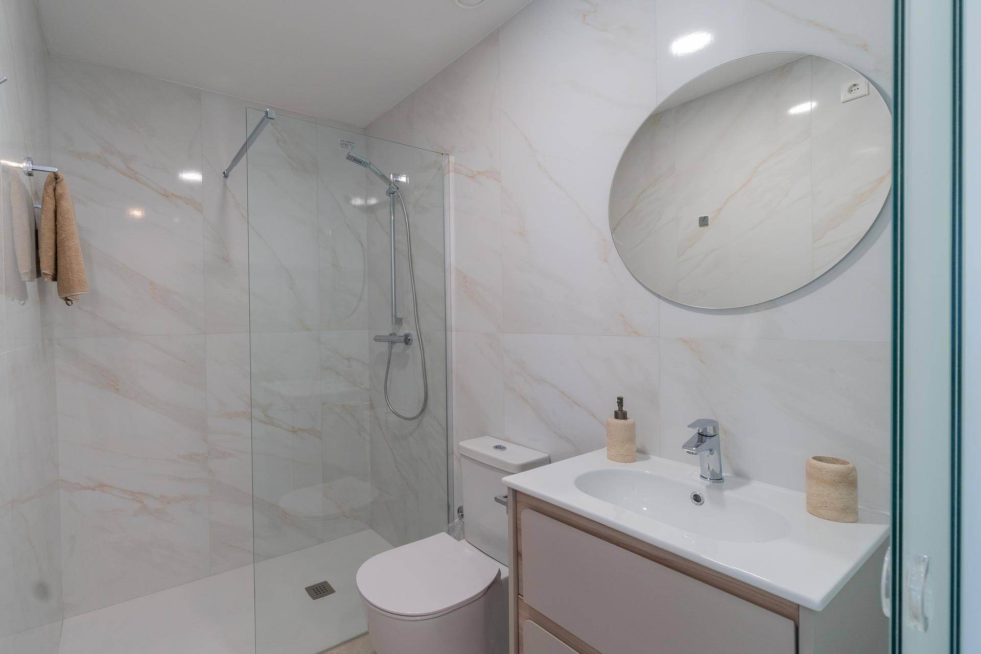 Elegantes Badezimmer mit Marmoroptik-Fliesen, moderner Dusche und Waschtisch mit rundem Spiegel.