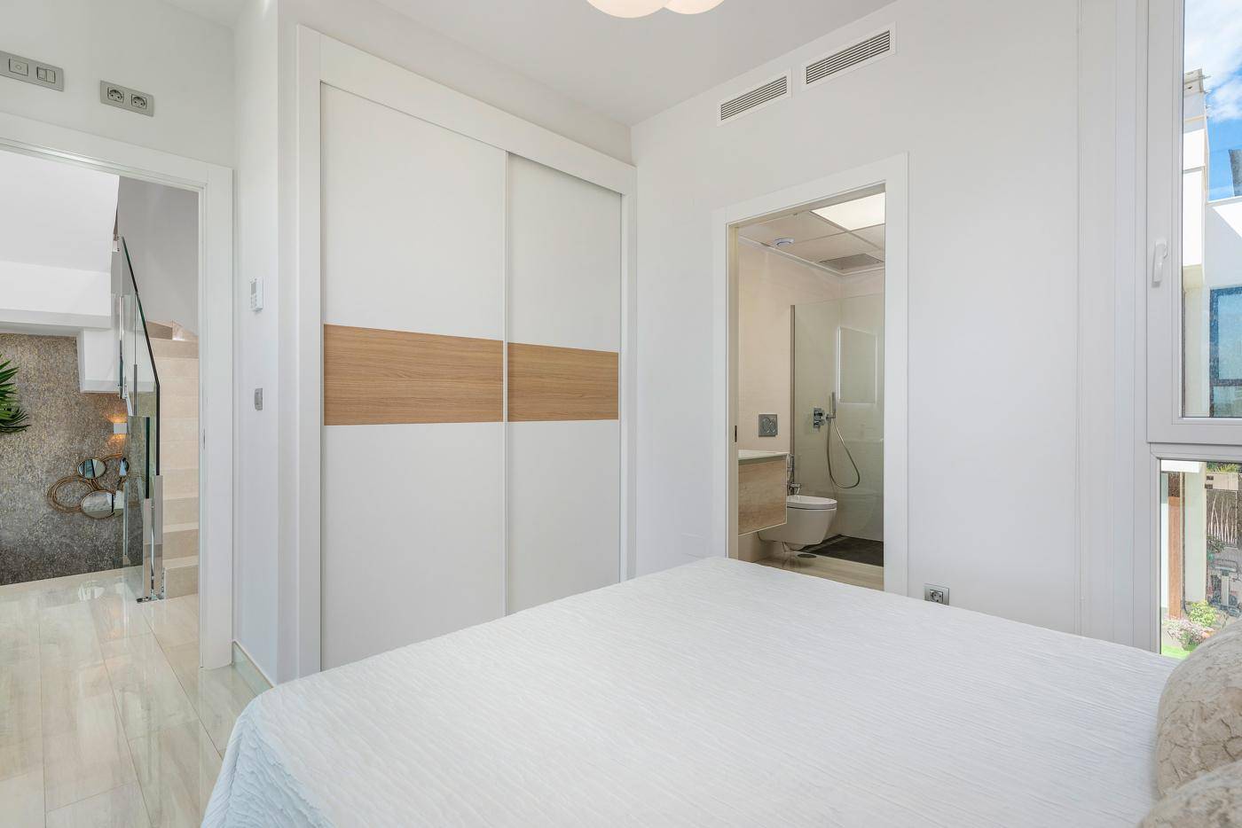 Schlafzimmer mit Zugang zu einem eigenen Badezimmer und integriertem Schrank, hell und modern.