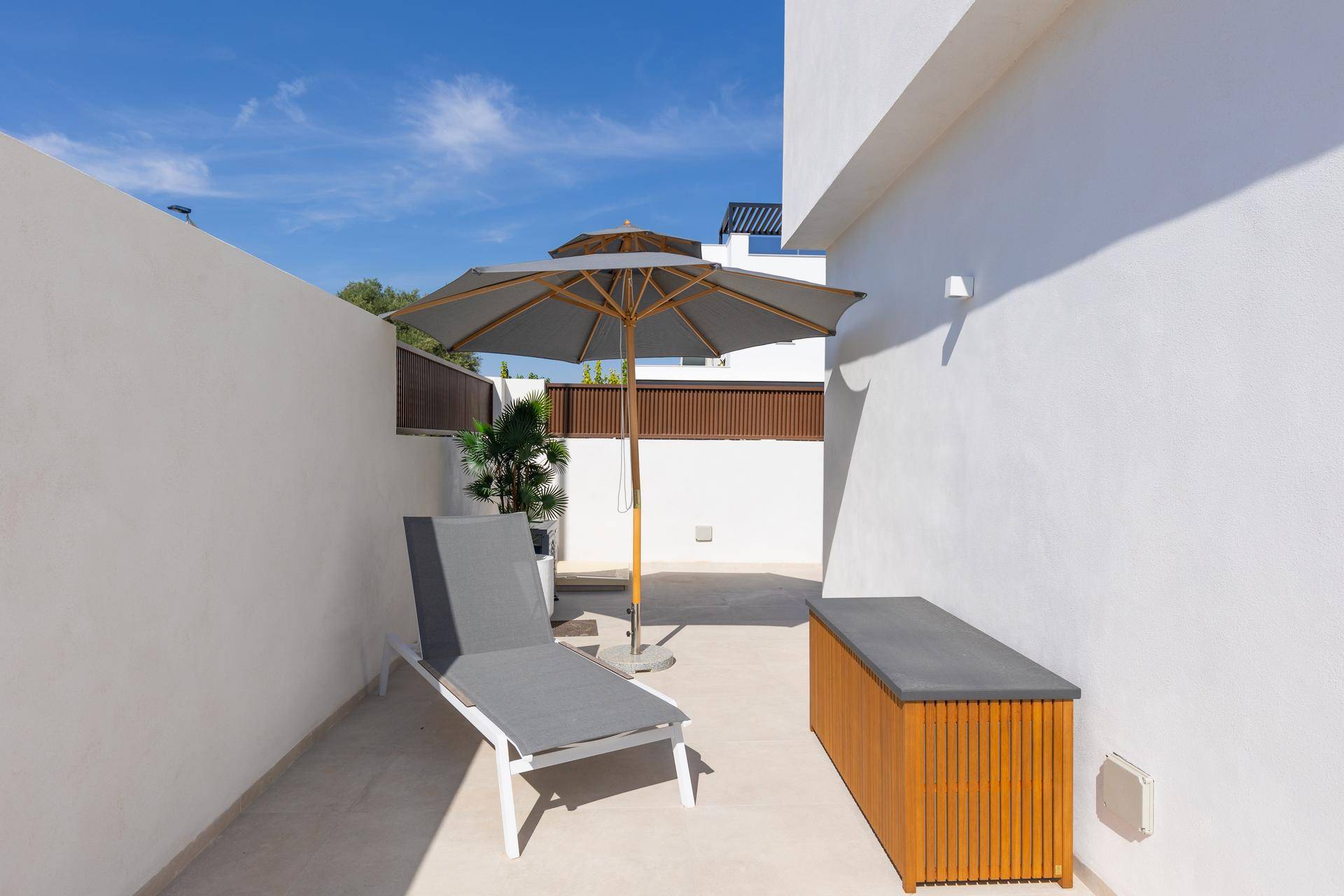 Schmaler, sonniger Patio-Bereich mit Liegestuhl und Sonnenschirm an der Hauswand.