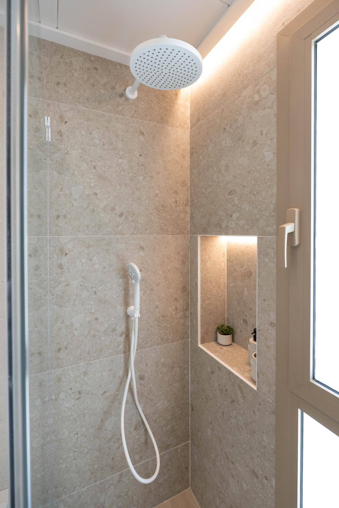 Moderne Dusche mit Regenduschkopf, Nische für Utensilien und Fenster für Tageslicht.