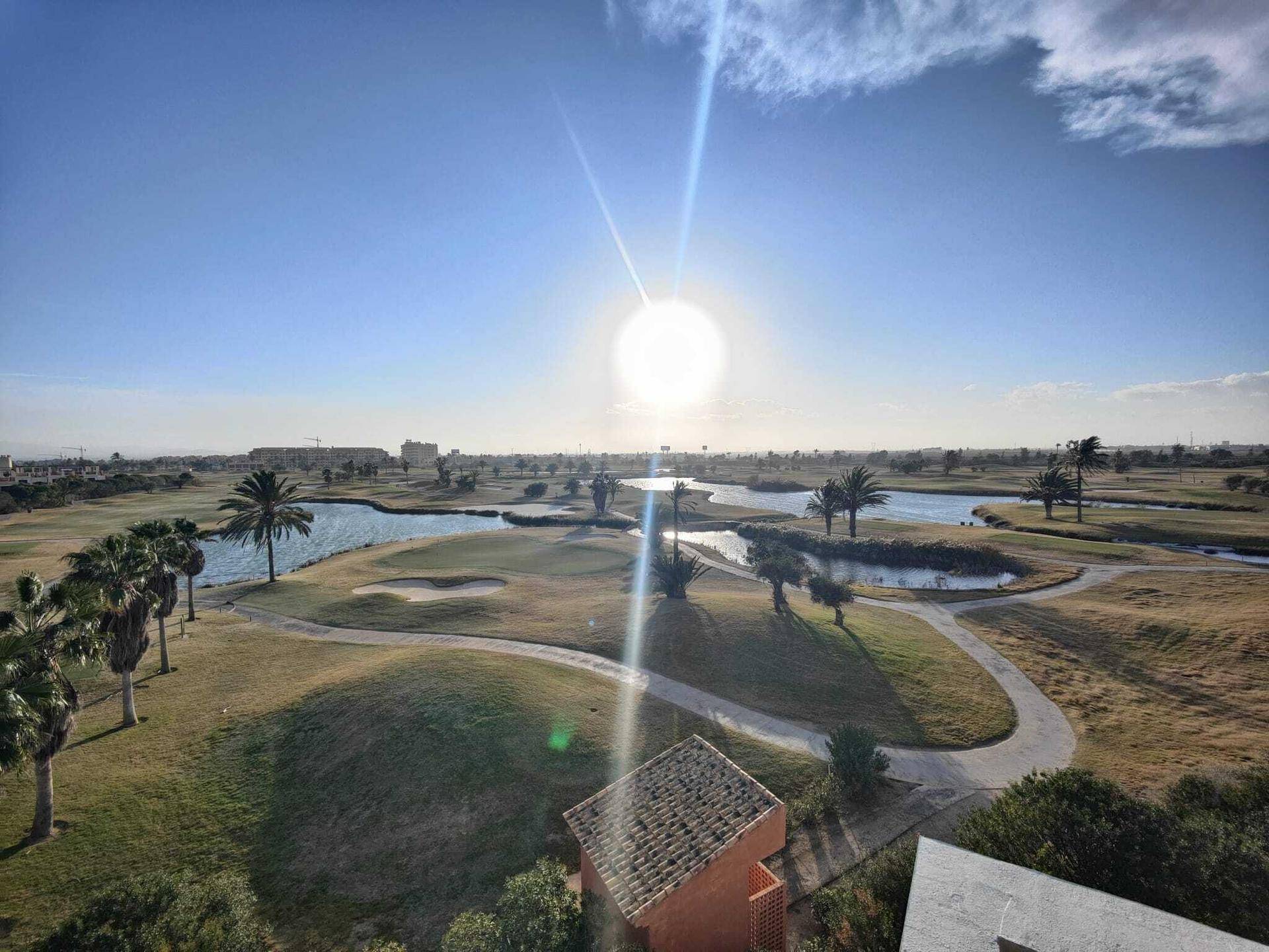 Weitläufiger Golfplatz mit Wasserhindernissen und Palmen unter strahlendem Sonnenschein.