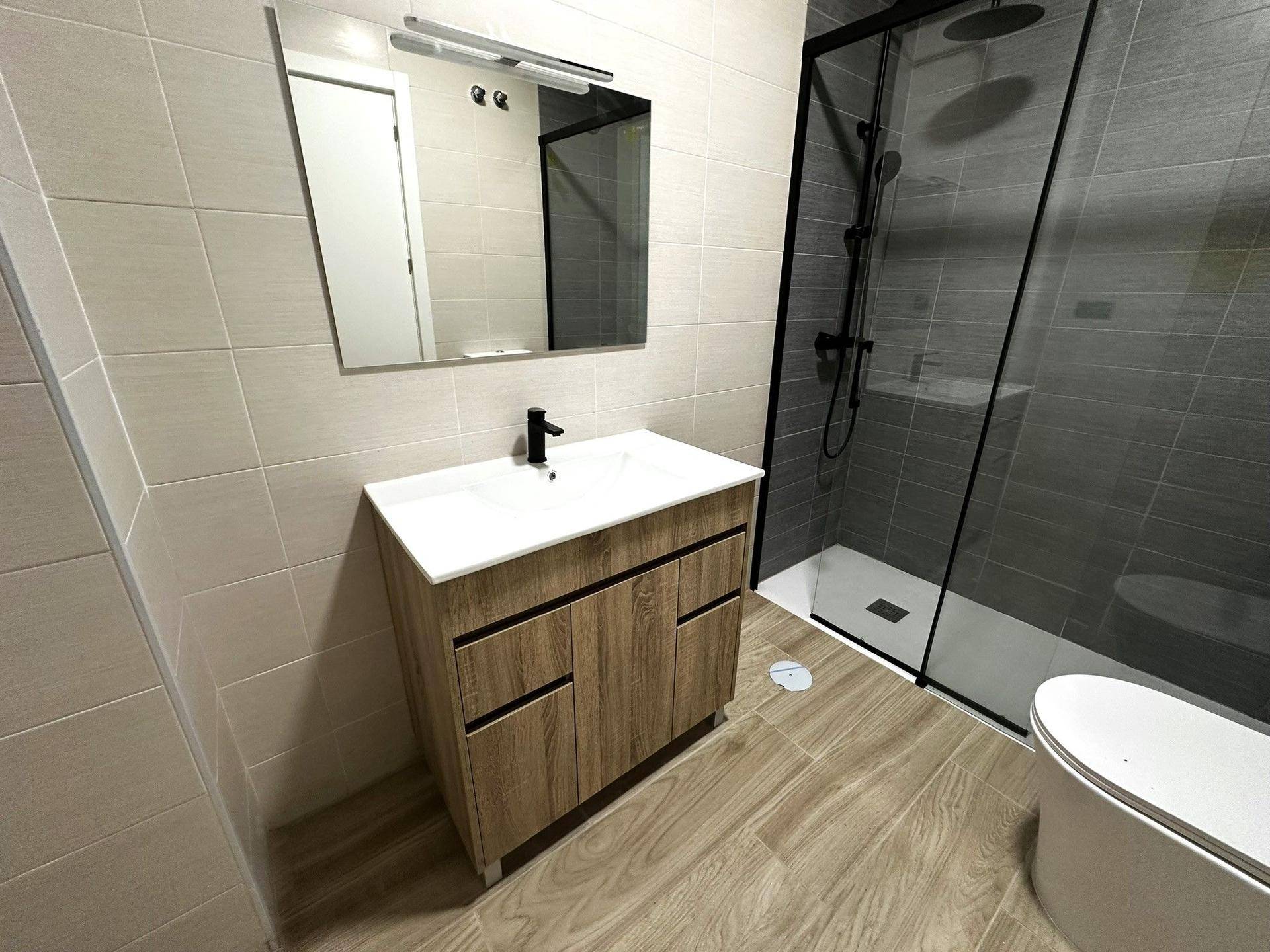 Zeitgemäßes Badezimmer mit Holzwaschtisch, großem Spiegel und geräumiger Duschkabine.