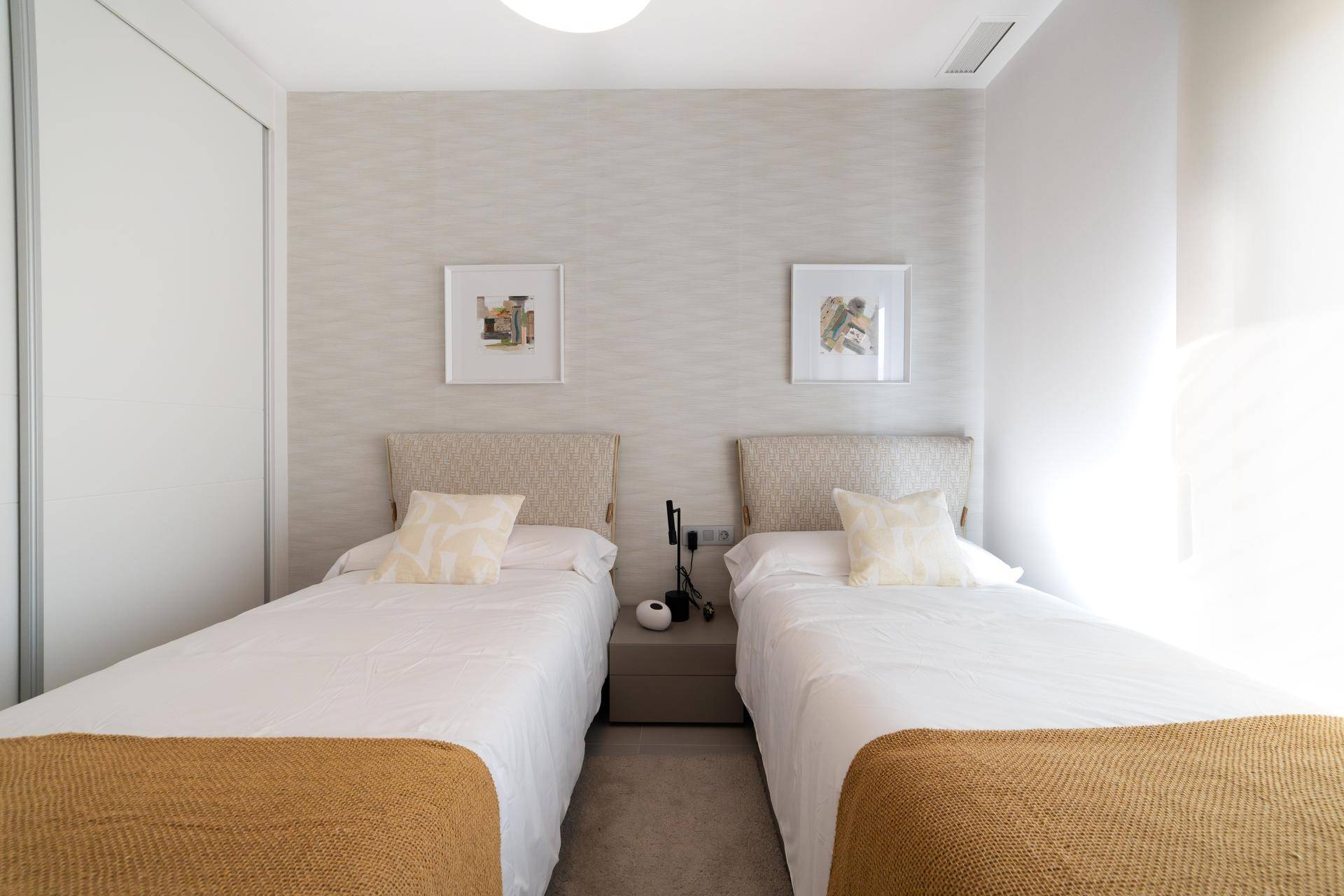 Helles Schlafzimmer mit zwei Einzelbetten, schlichter Dekoration und Einbauschränken.