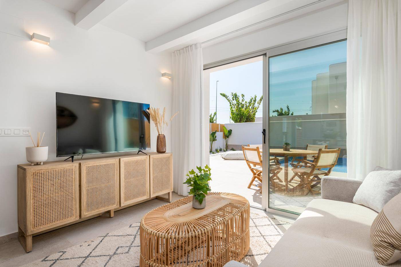 Helles Wohnzimmer mit TV-Möbel, Sofa und Blick auf den Außenbereich mit Pool.
