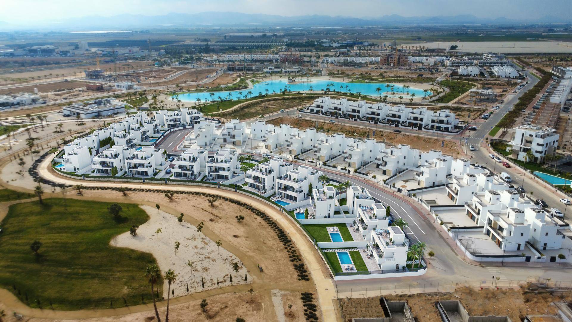 Weitläufige Luftaufnahme einer neuen Wohnsiedlung mit vielen Häusern, Pools und einer künstlichen Lagune.