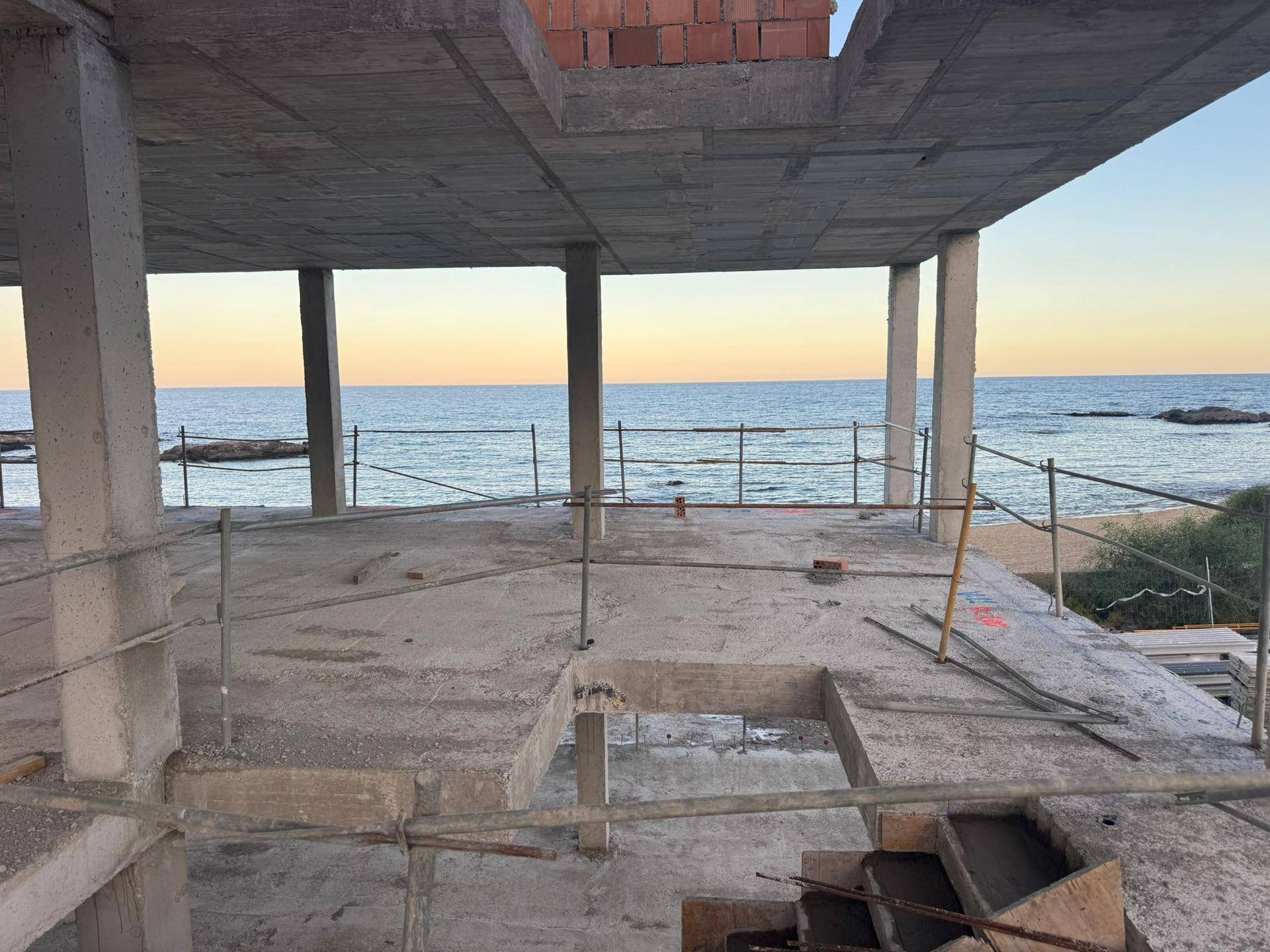 Baustelle mit Blick auf das Meer, zeigt die Rohbaukonstruktion mit Betonpfeilern und -decken.