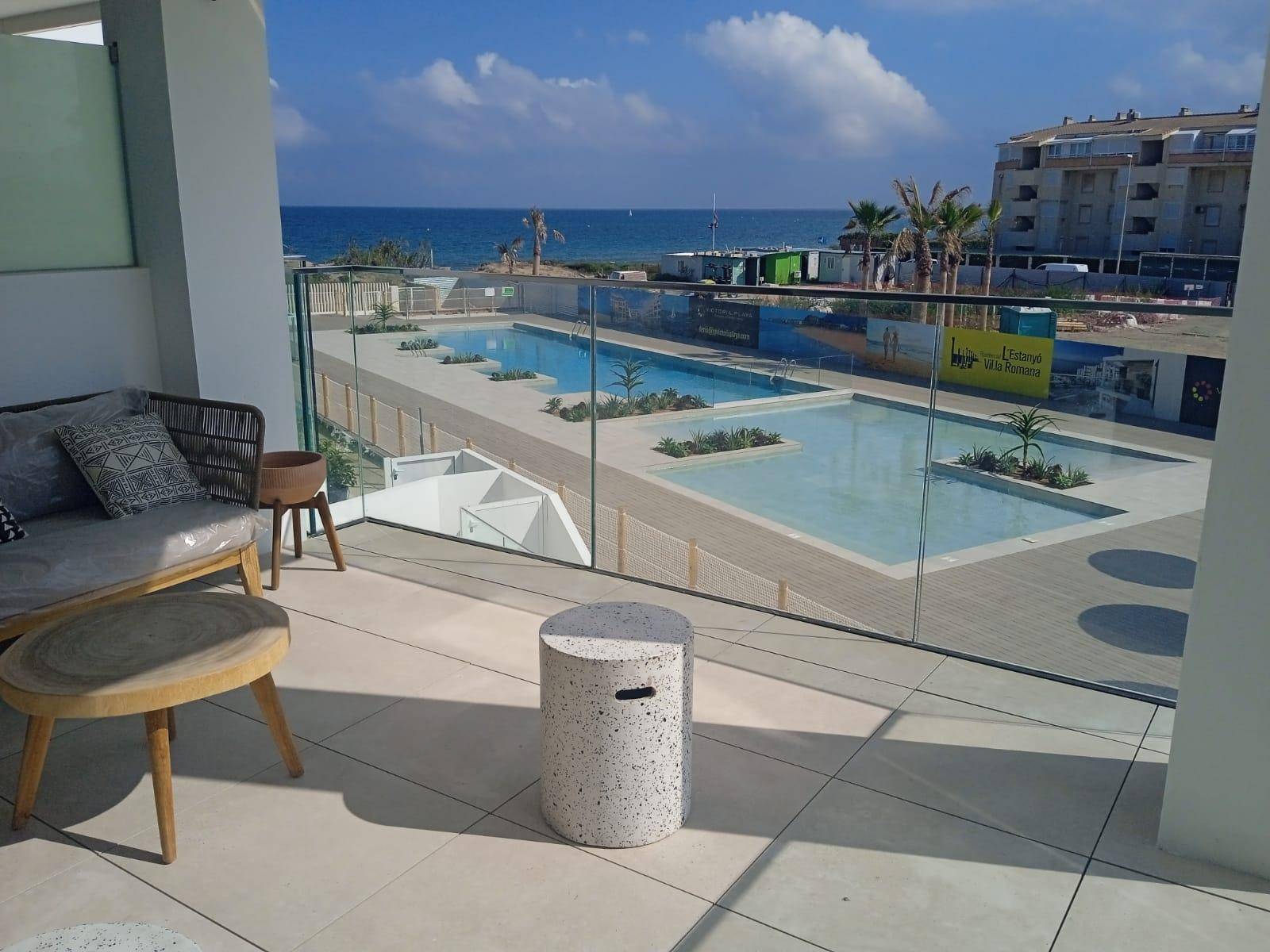 Möblierter Balkon mit Glasgeländer bietet Blick auf den Poolbereich und das Meer.