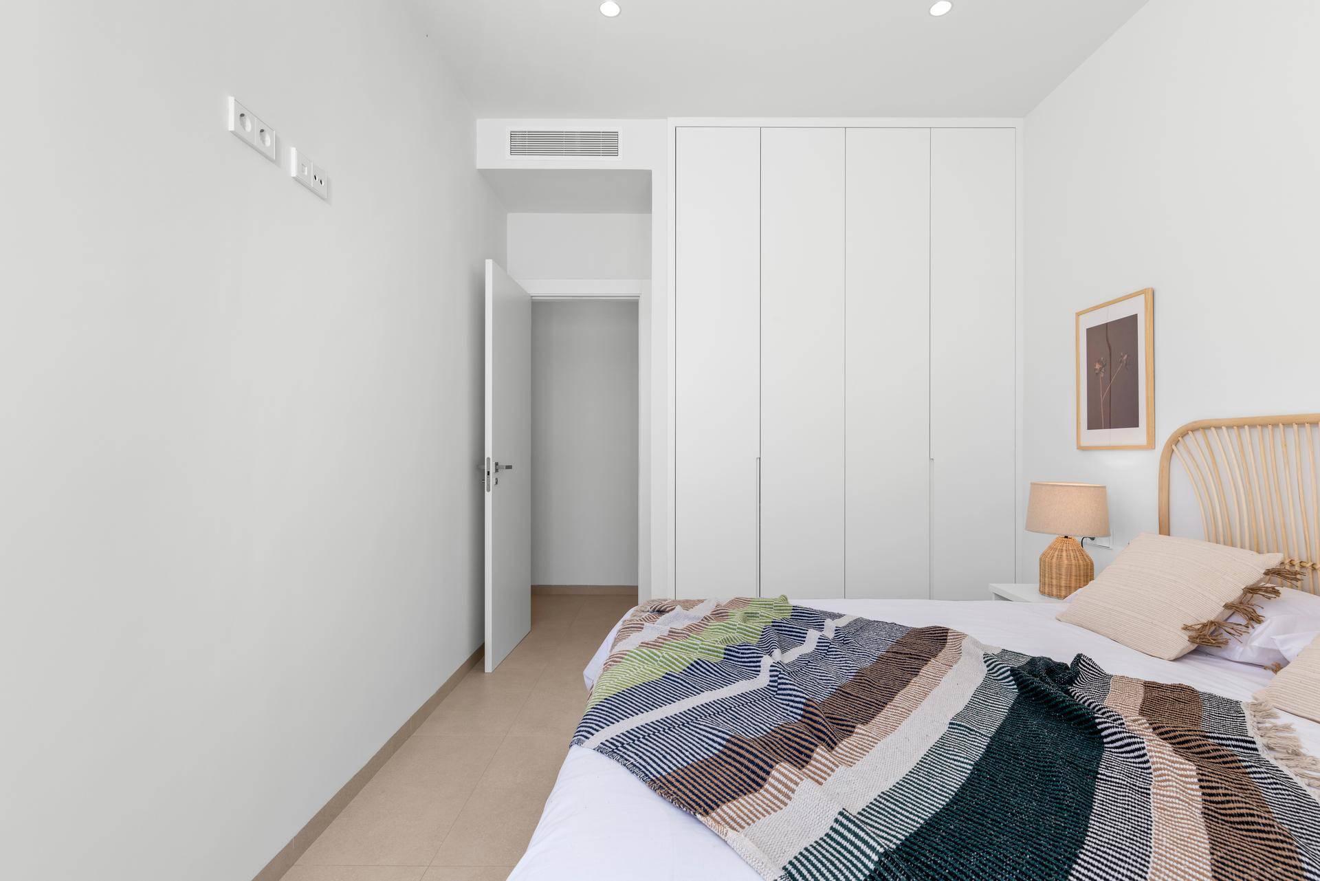 Helles Schlafzimmer mit Einbauschränken, modernem Bett und Zugang zu einem weiteren Raum.