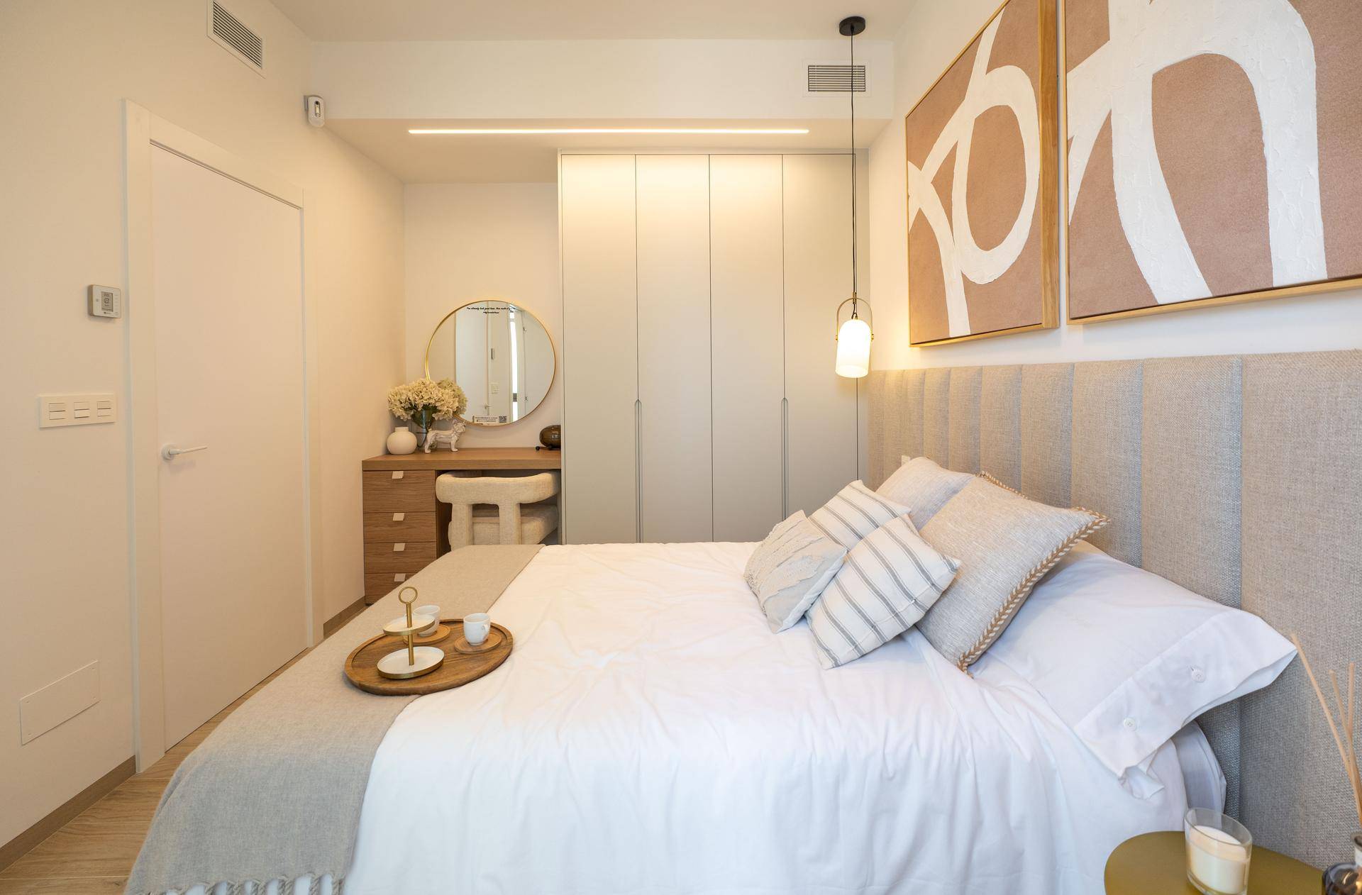 Modernes Schlafzimmer mit beigem Kopfteil, Einbauschränken und einem runden Spiegel.
