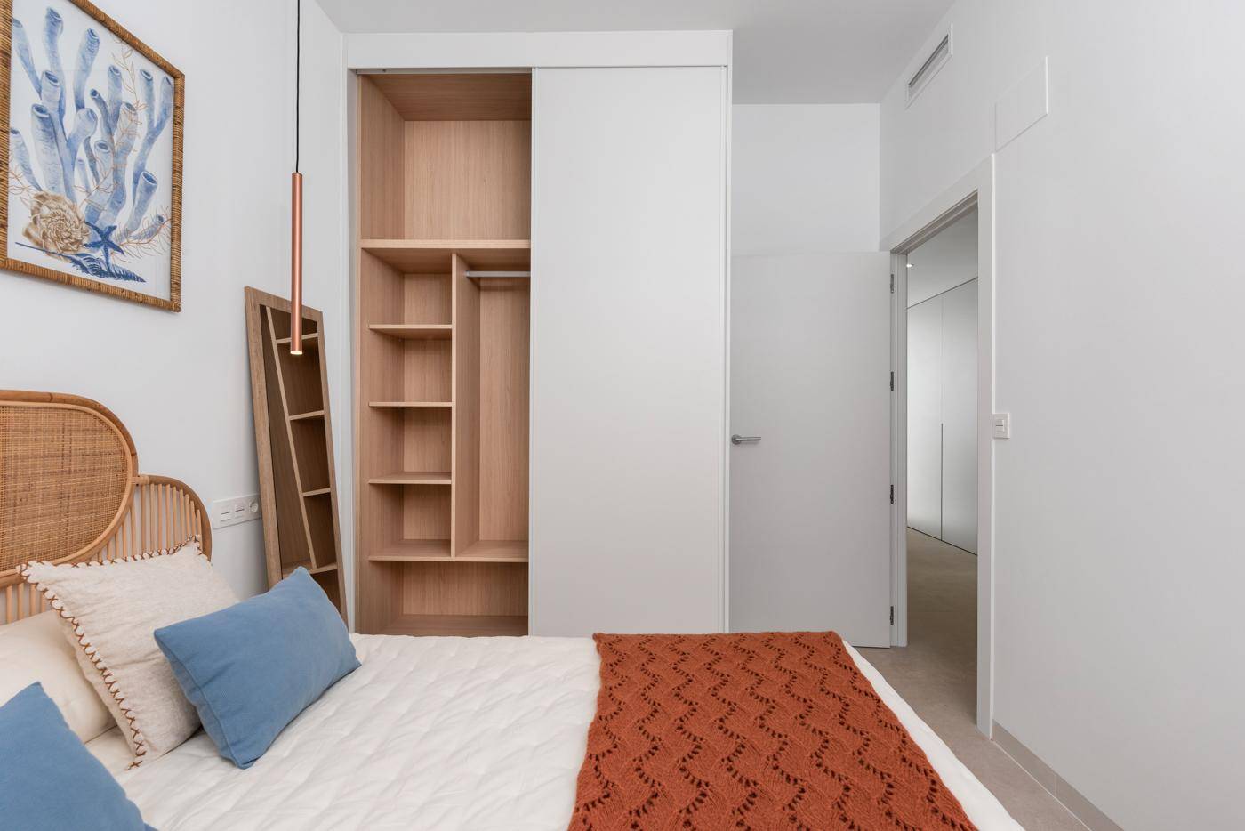 Schlafzimmer mit offenem Kleiderschrank, Rattan-Kopfteil und moderner Einrichtung.