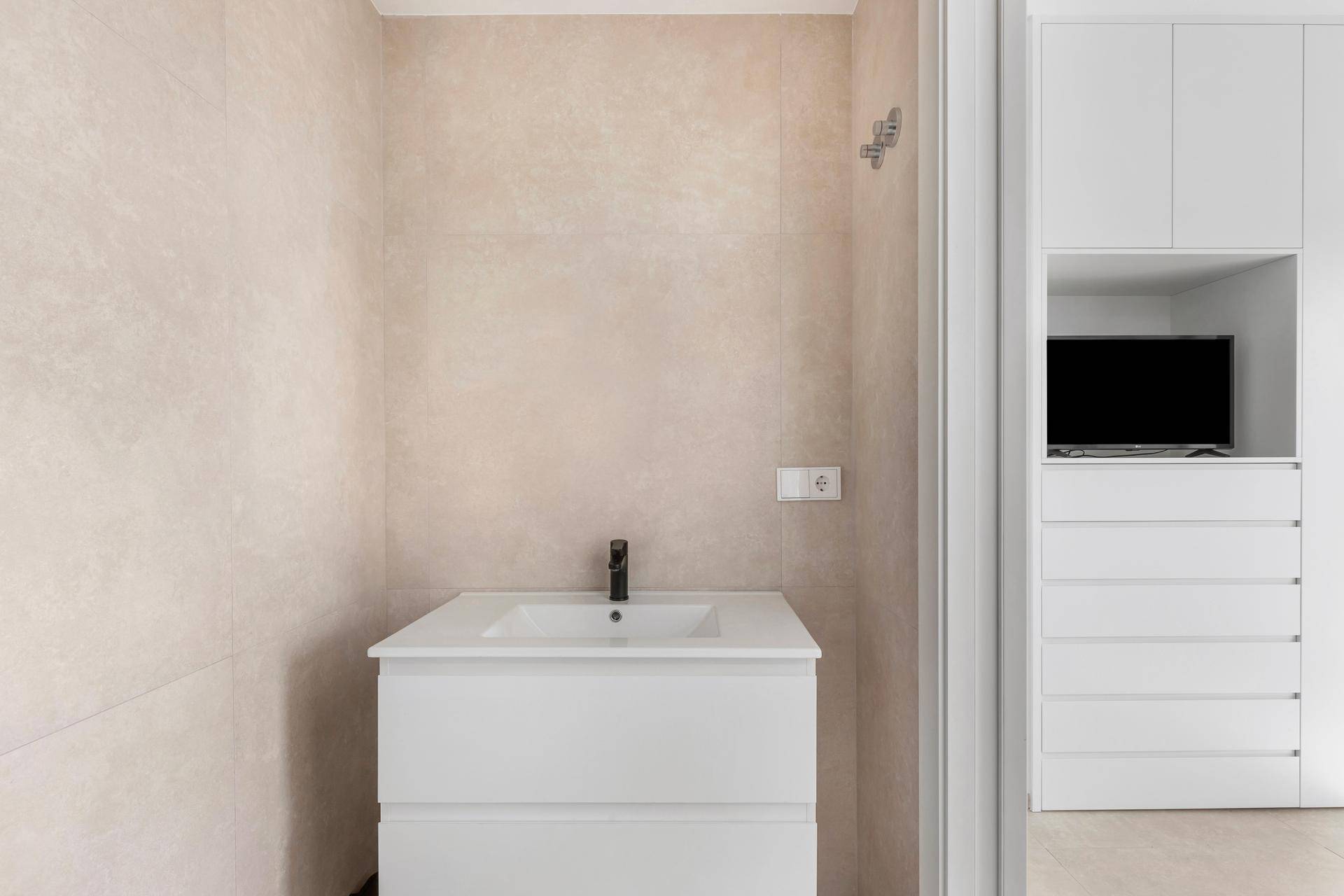 Modernes Badezimmer mit Waschtisch und hellen Fliesen, angrenzend an einen Schrankbereich.