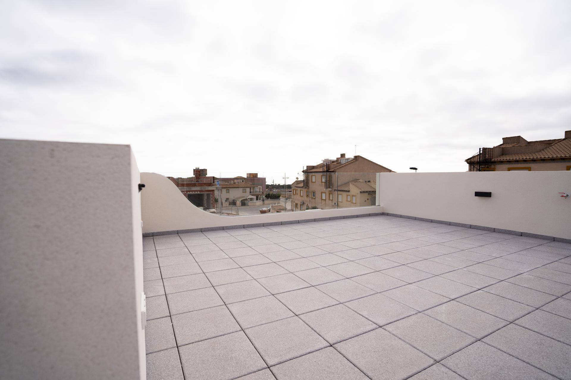 Geräumige Dachterrasse mit hellen Fliesen und Blick auf die Nachbarschaft.