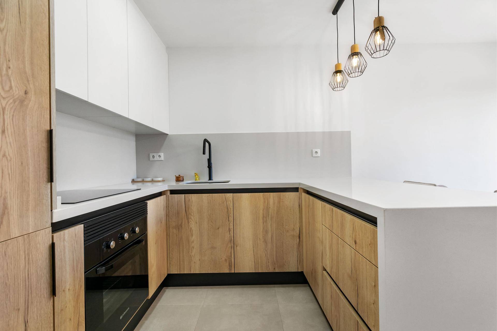 Moderne L-förmige Küche mit Holz- und weißen Schränken, integriertem Backofen und heller Arbeitsplatte.
