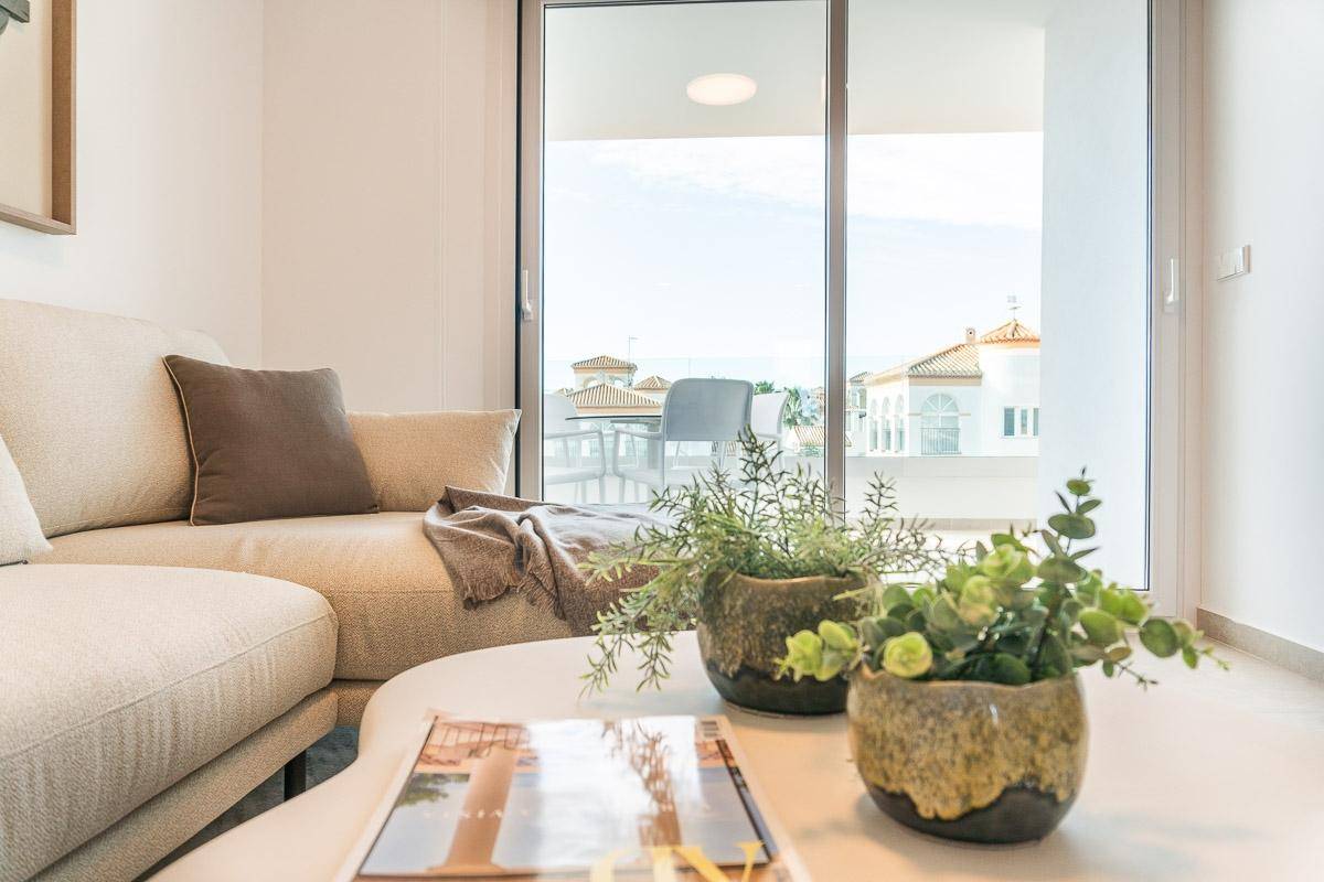 Helles Wohnzimmer mit beigem Sofa, Couchtisch und Zugang zu einem Balkon mit Blick auf die Umgebung.