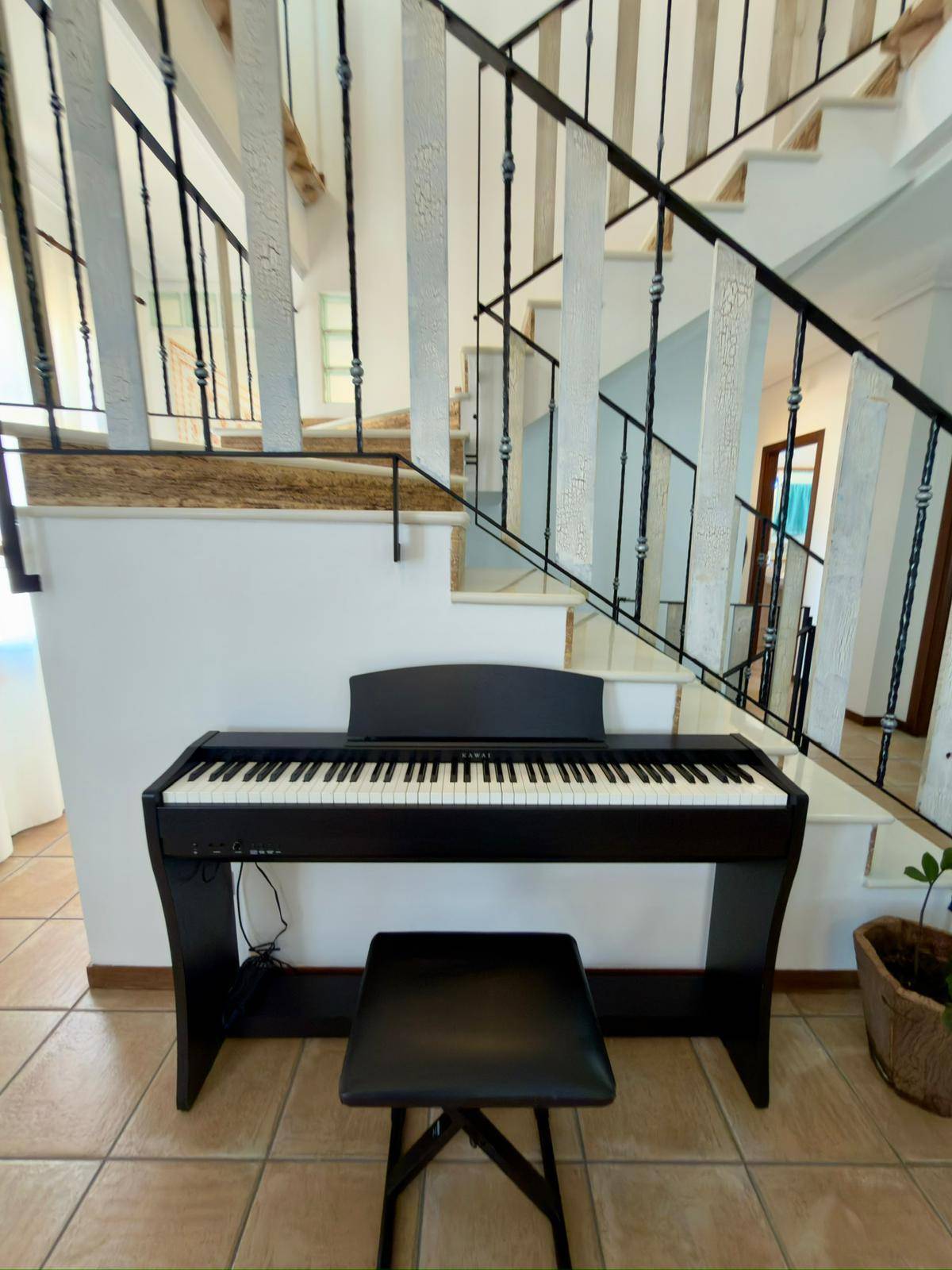Detailansicht der Treppe mit schmiedeeisernem Geländer und einem Klavier im Flur.