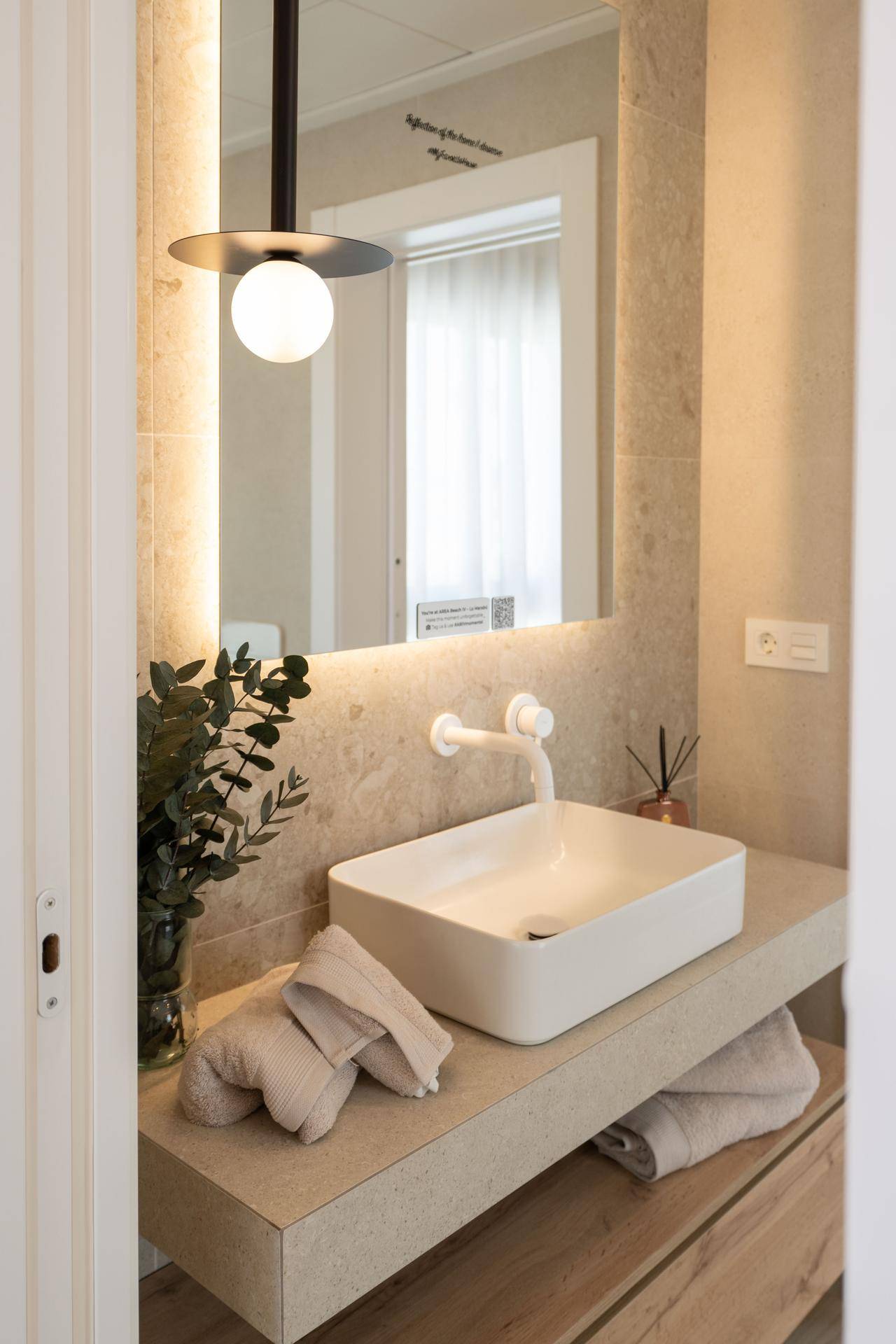 Detailansicht des Einzelwaschbeckens mit beleuchtetem Spiegel und moderner Armatur.