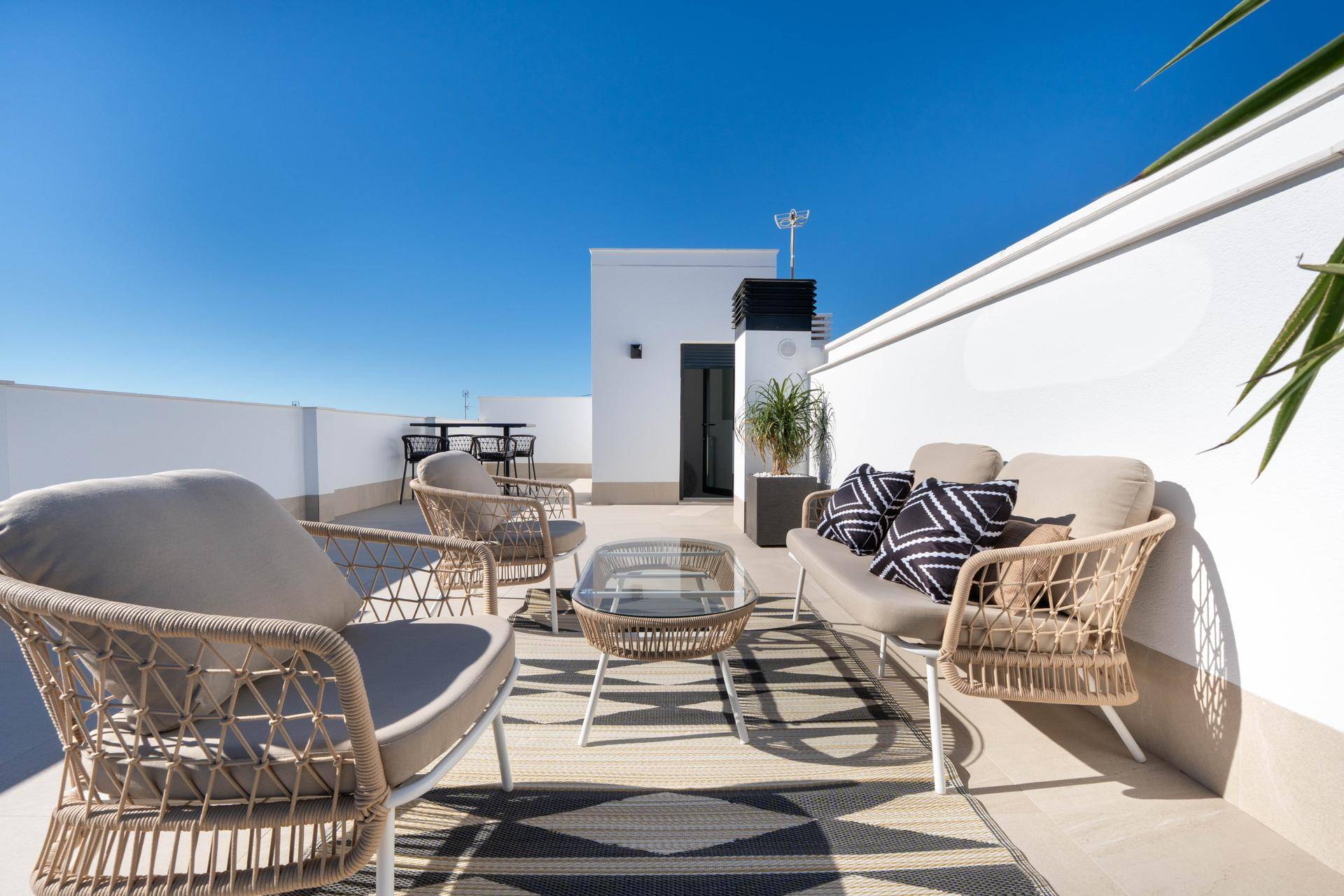 Sonnige Dachterrasse mit bequemen Outdoor-Möbeln und weitem Blick unter blauem Himmel.