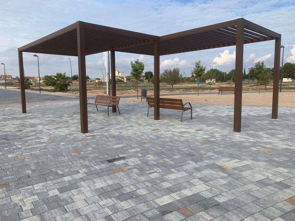 Öffentlicher Parkbereich mit Pergola, Sitzbänken und gepflastertem Boden.
