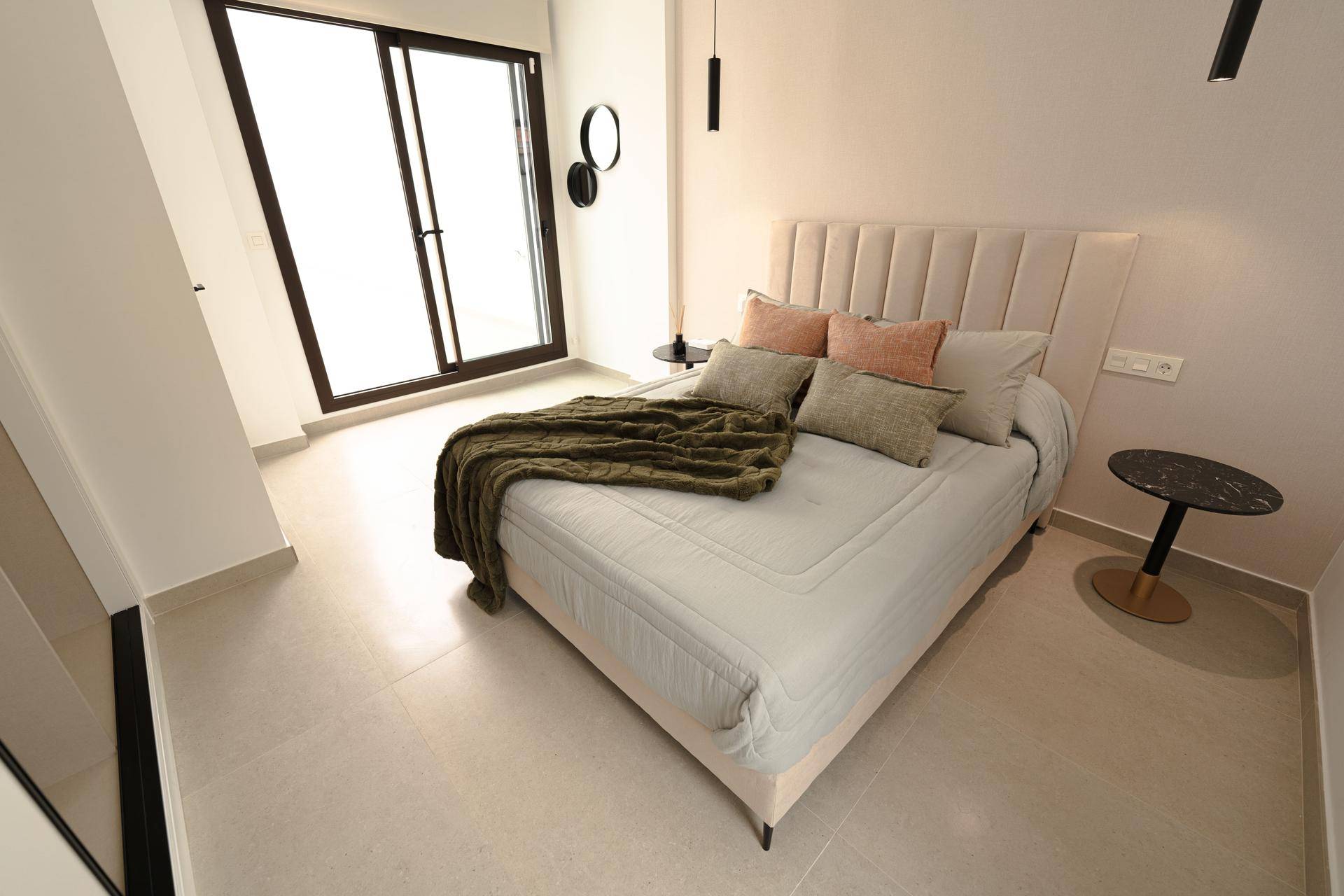 Helles Schlafzimmer mit bequemem Bett und großen Glasschiebetüren, die viel Tageslicht hereinlassen.