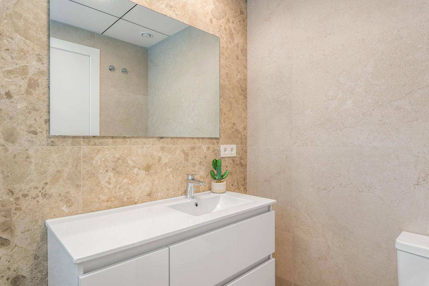 Modernes Badezimmer mit Waschtisch, Spiegel und beigefarbenen Fliesen.