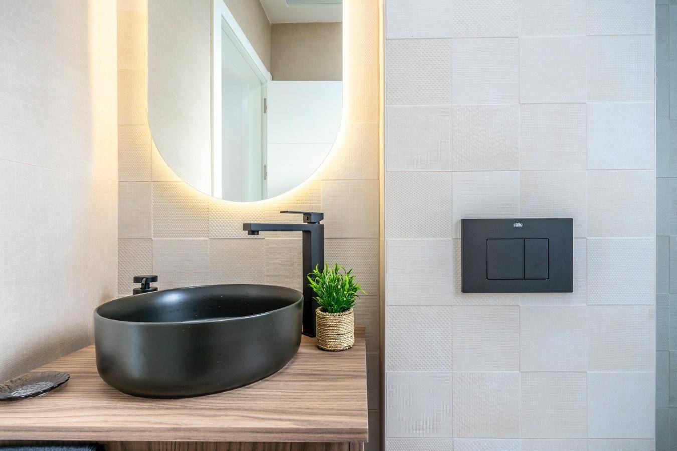 Detailansicht eines modernen Badezimmers mit schwarzem Aufsatzwaschbecken, Holzunterschrank und beleuchtetem Spiegel.