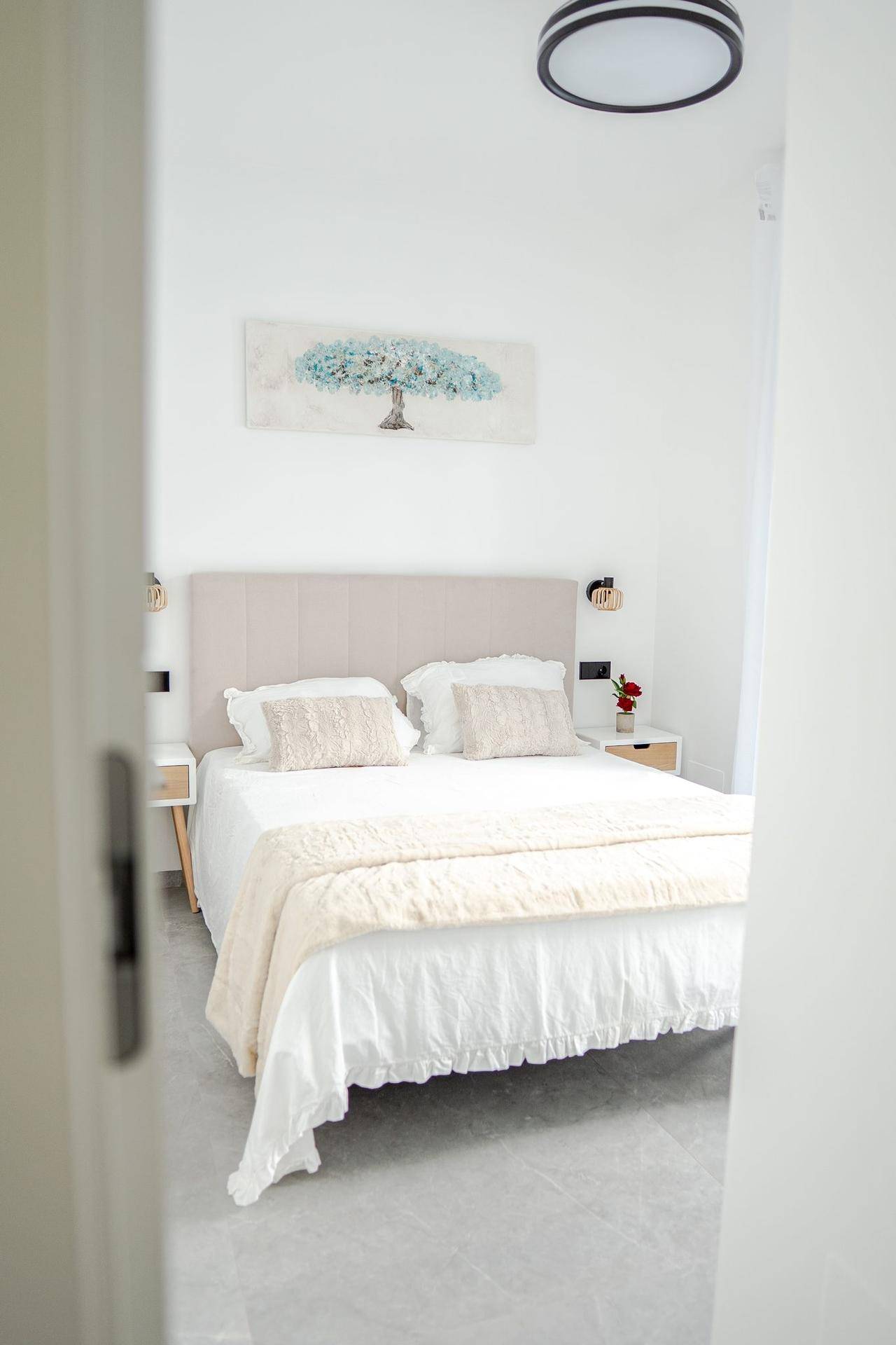 Helles Schlafzimmer mit Doppelbett, gepolstertem Kopfteil und einem modernen Kunstwerk.