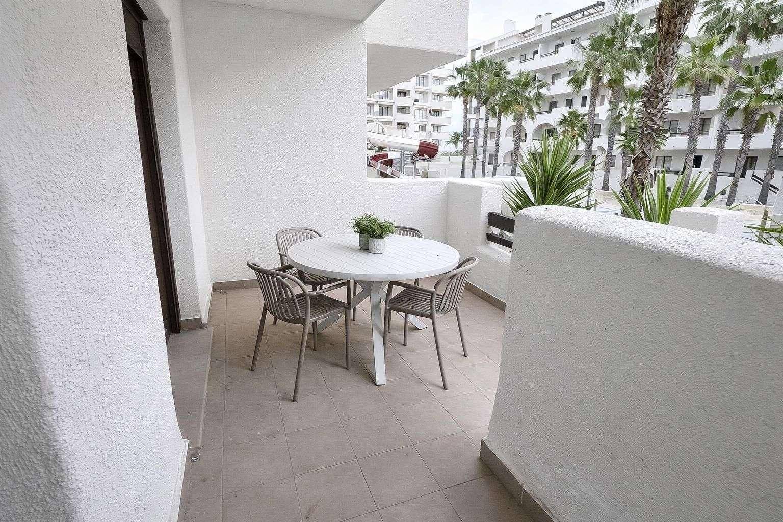 Möblierter Balkon mit Tisch und Stühlen, Blick auf andere Gebäude und Palmen.