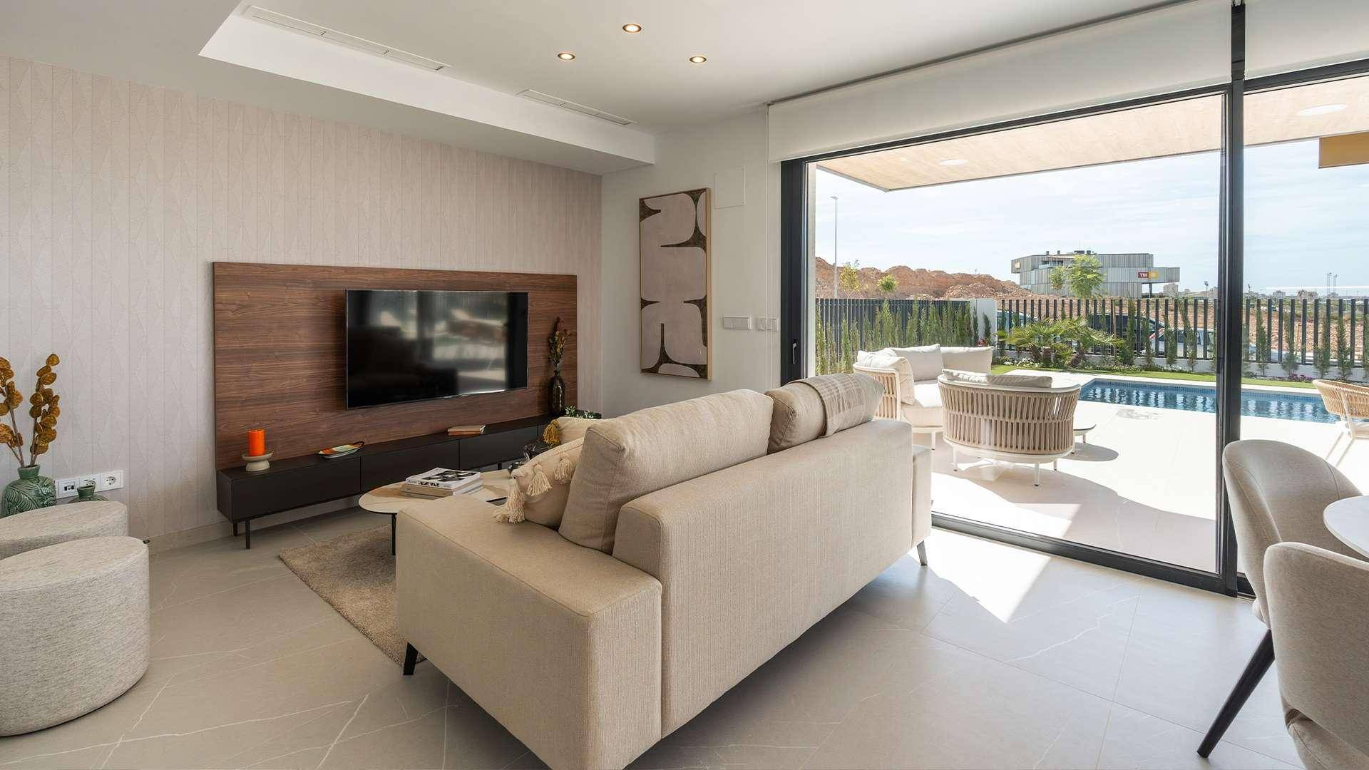 Modernes Wohnzimmer mit Fernseher, beigem Sofa und großem Schiebefenster zur Terrasse.