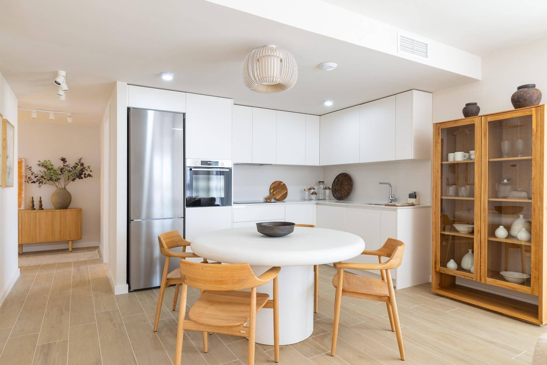 Moderne weiße Küche mit Essbereich, Holztisch und integrierten Edelstahlgeräten.