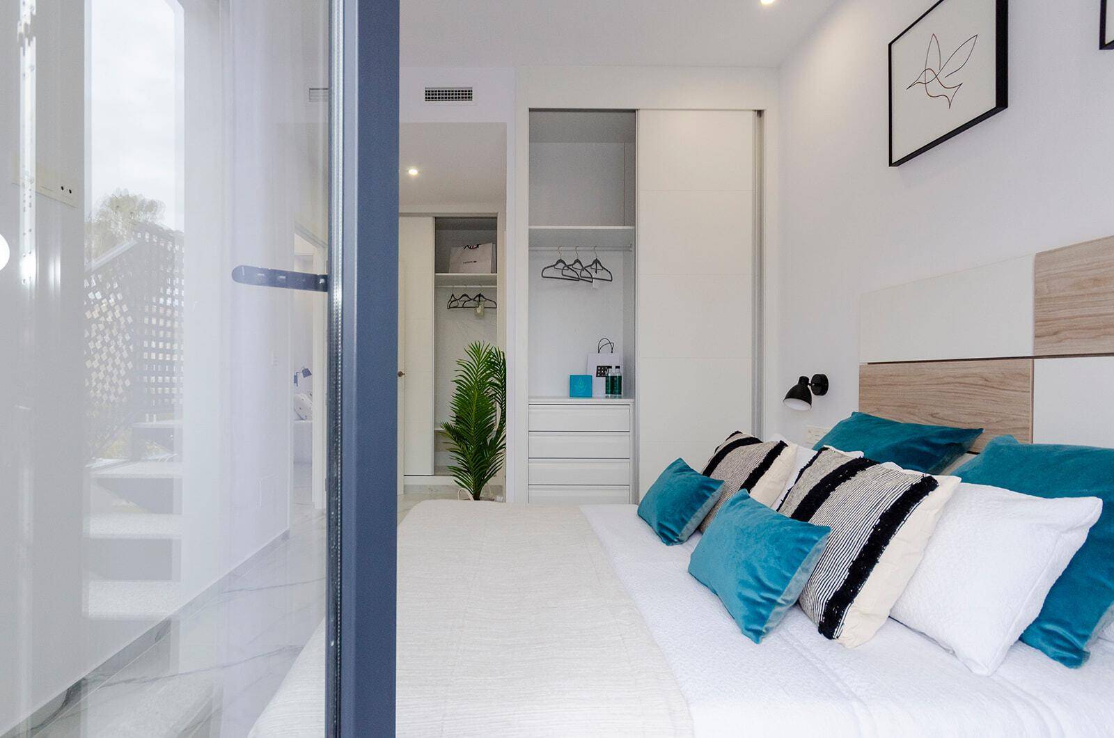 Helles Schlafzimmer mit Doppelbett und integriertem Kleiderschrank, durch eine Tür sichtbar.