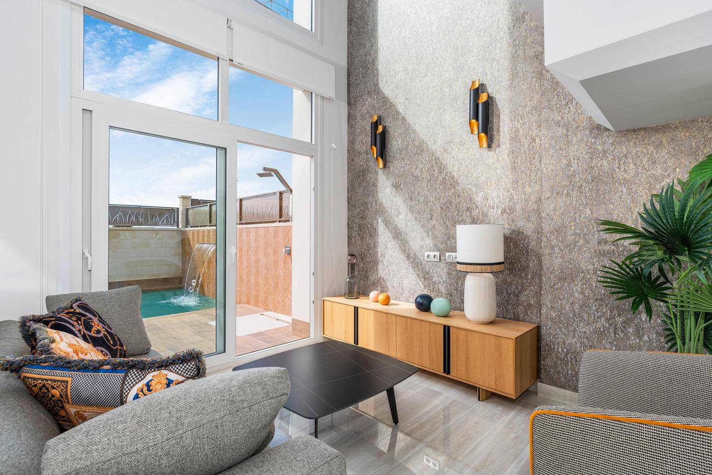 Modernes Wohnzimmer mit strukturierter Wand, stilvollen Leuchten und direktem Zugang zum Poolbereich.