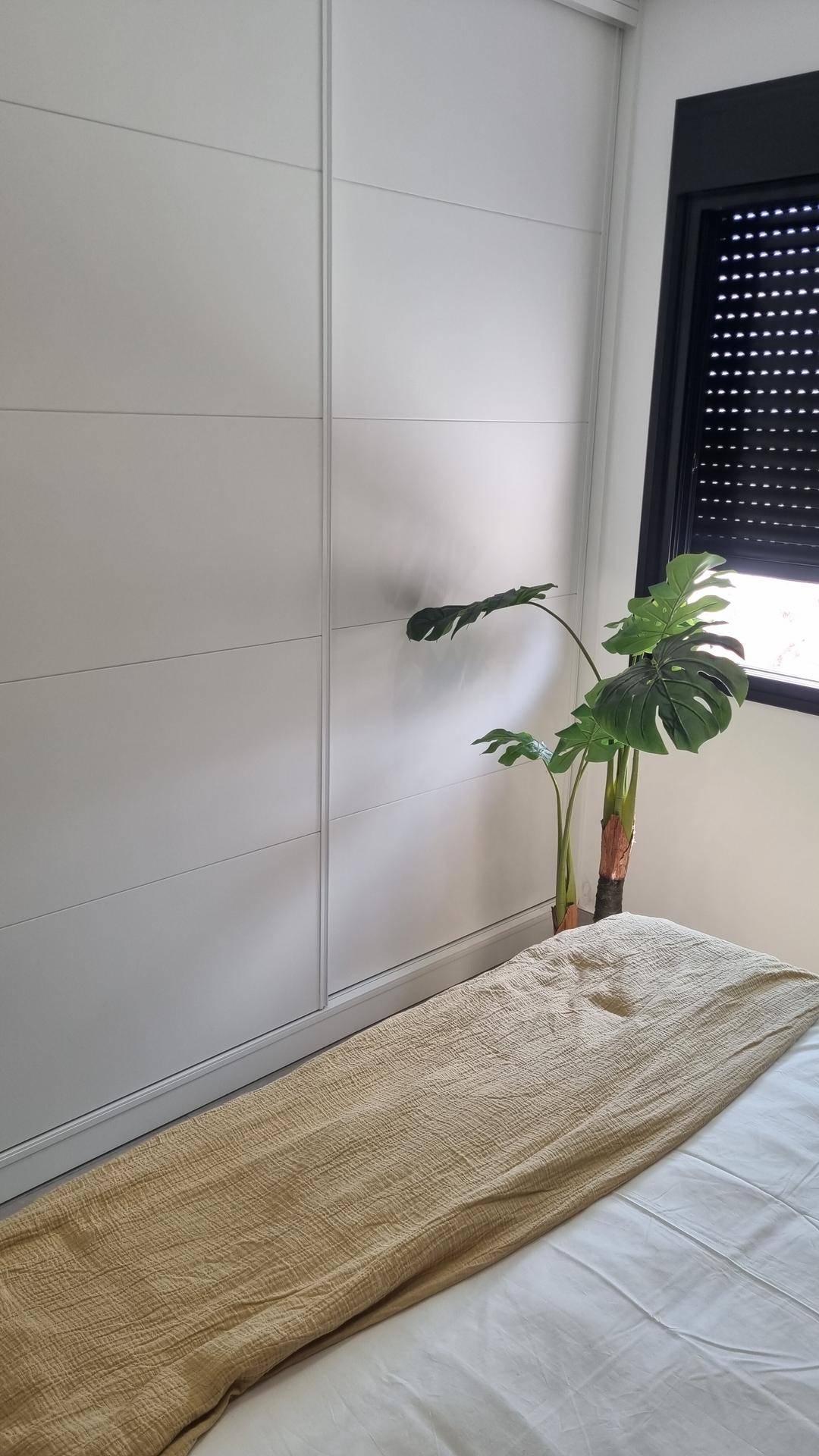 Helles Schlafzimmer mit Einbauschränken, Fenster und einer Zimmerpflanze.