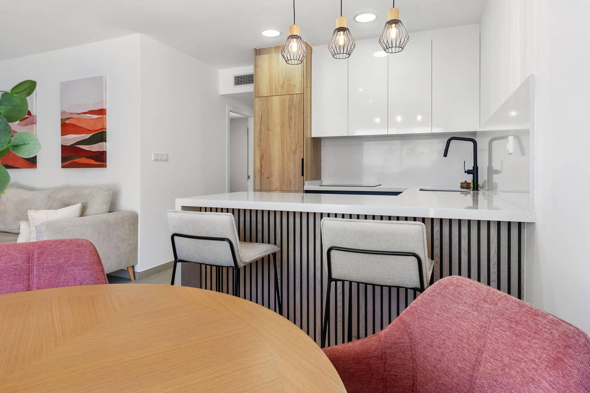 Moderner Essbereich mit Holztisch, rosa Stühlen und offener Küche mit Frühstücksbar.