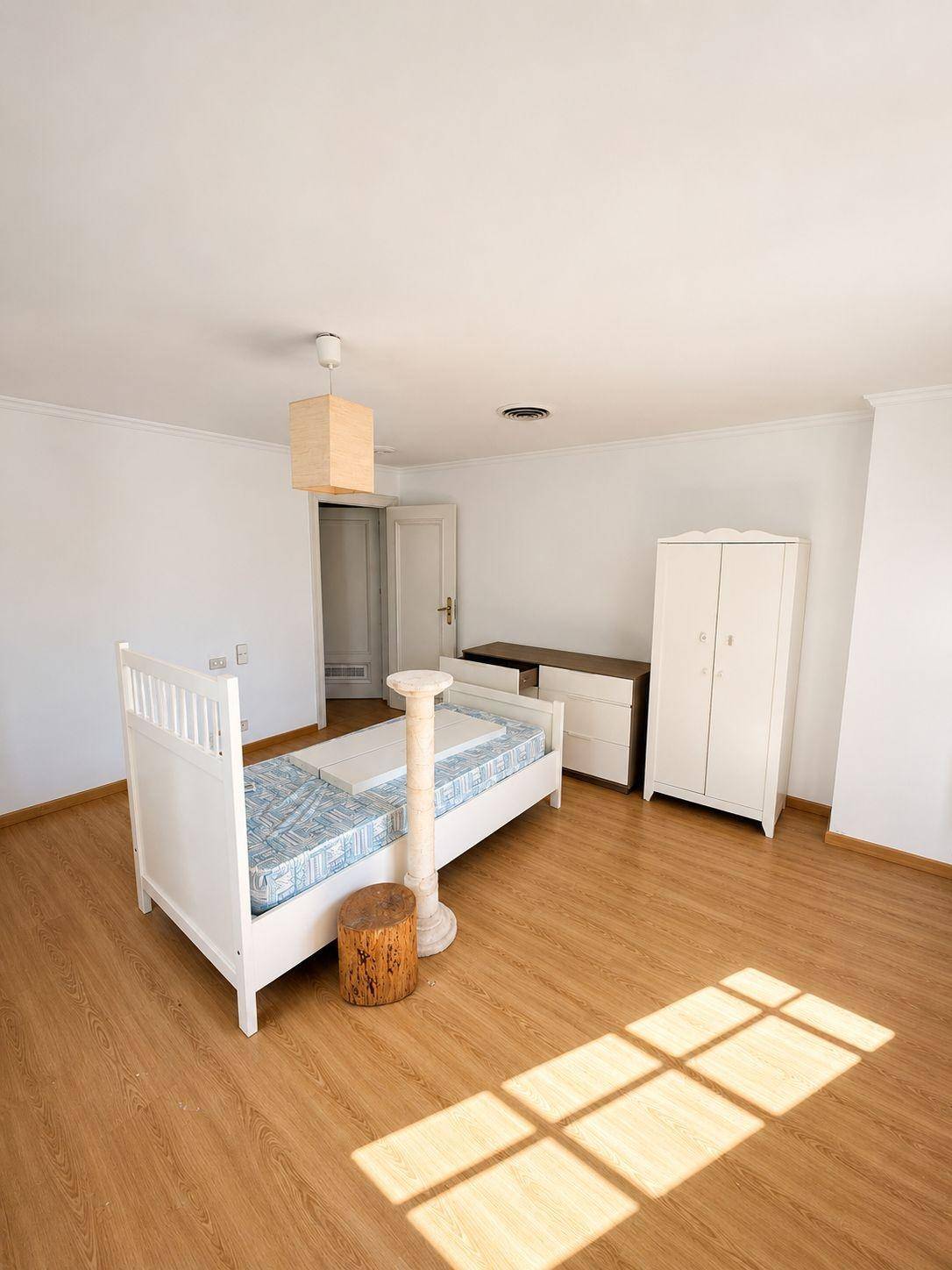 Helles Schlafzimmer mit Laminatboden, weißem Bett und Kleiderschrank, durchflutet von Sonnenlicht.