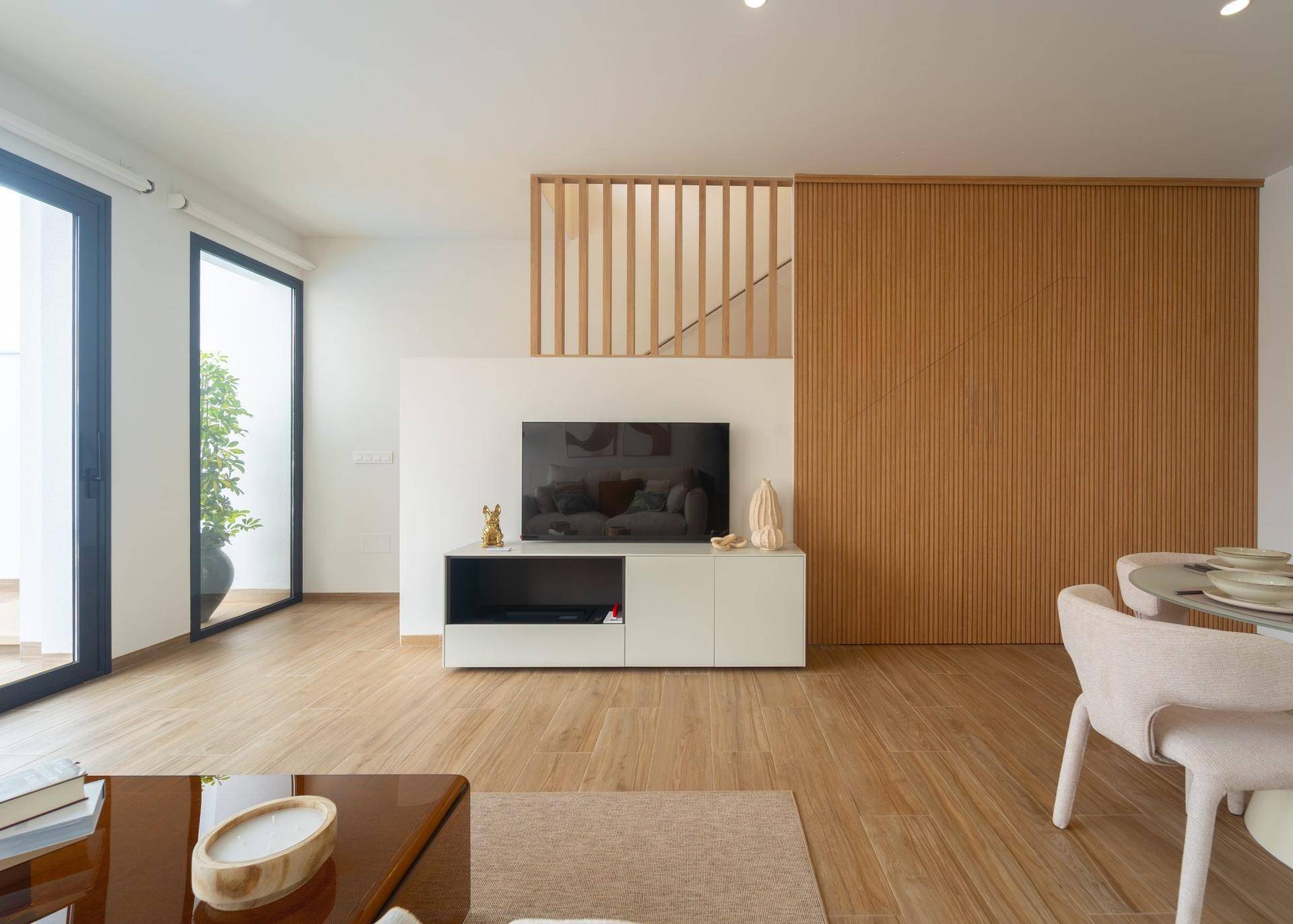 Helles Wohnzimmer mit Holzboden, moderner TV-Wand und Zugang zu einer Terrasse.